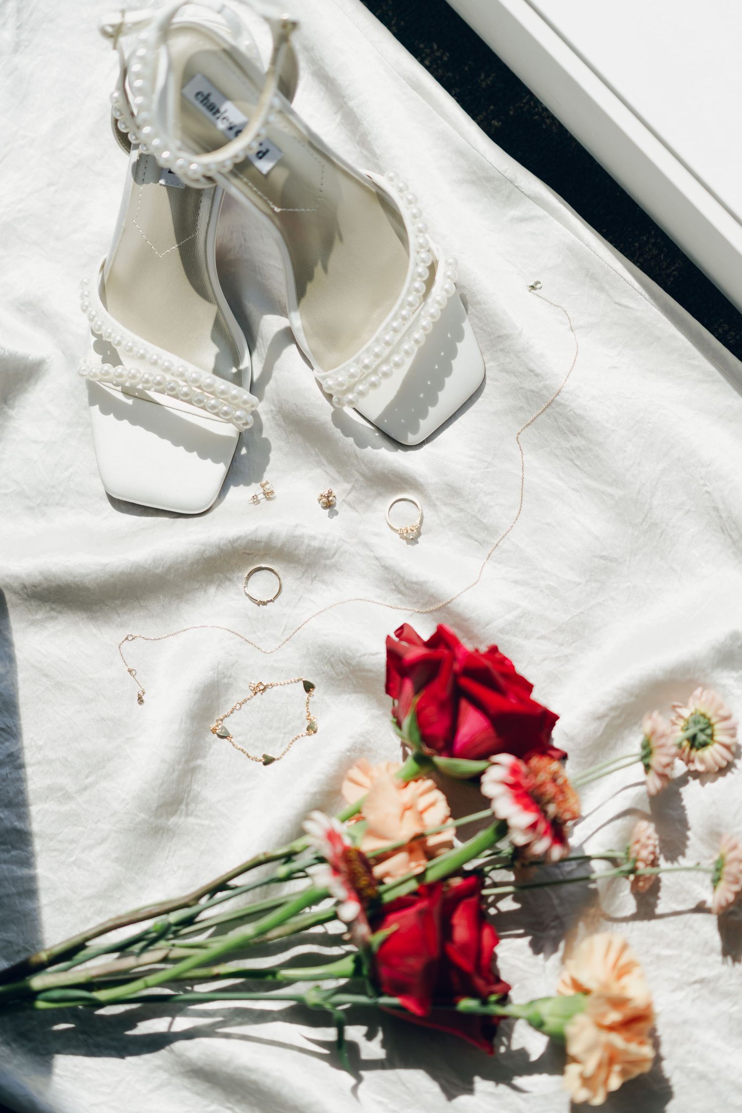 White wedding shoes and red roses arranged artistically on a light background in Halifax, Nova Scotia.