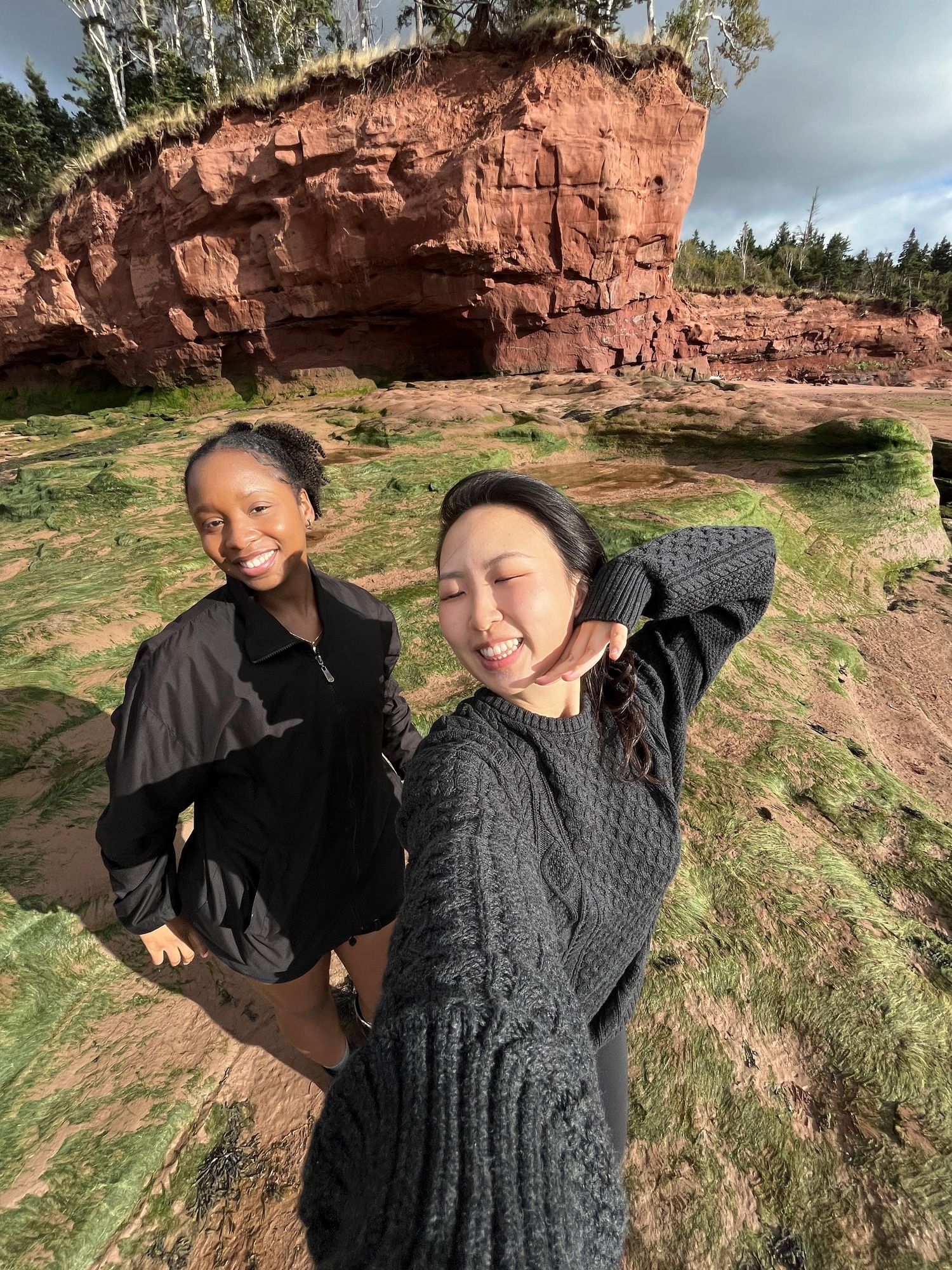 Two friends share joyful laughter while exploring red sandstone cliffs on a sunny outdoor adventure in Nova Scotia.