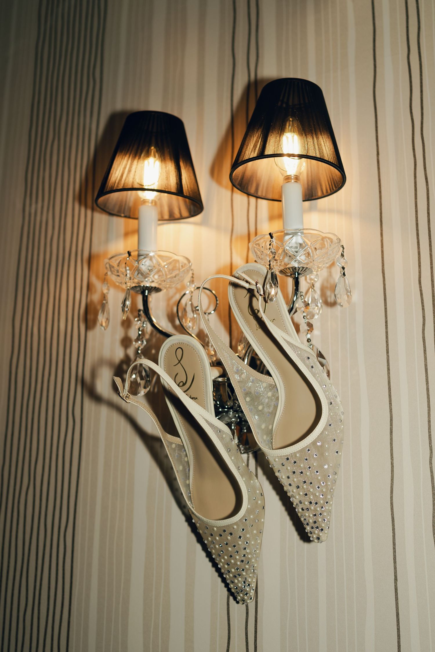 Elegant crystal wall sconces with black lampshades cast a warm glow against a striped wallpaper background at Lord Nelson Hotel, Halifax, NS