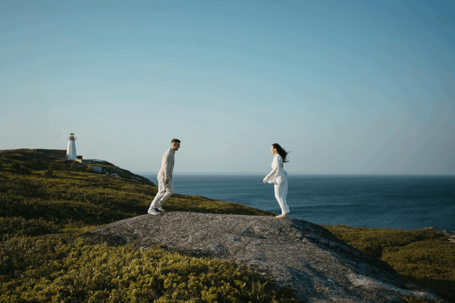 A couple stands at a scenic coastal cliff overlooking the ocean during a wedding photo session in Halifax, Nova Scotia.