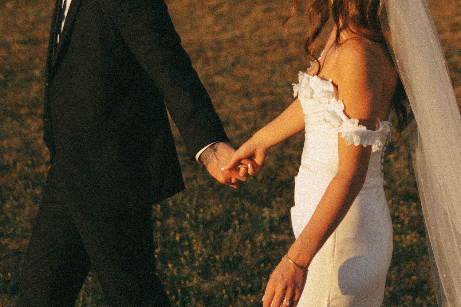 A bride in a white lace wedding dress holds a bouquet of white and pink roses against a rustic backdrop in Halifax, Nova Scotia.
