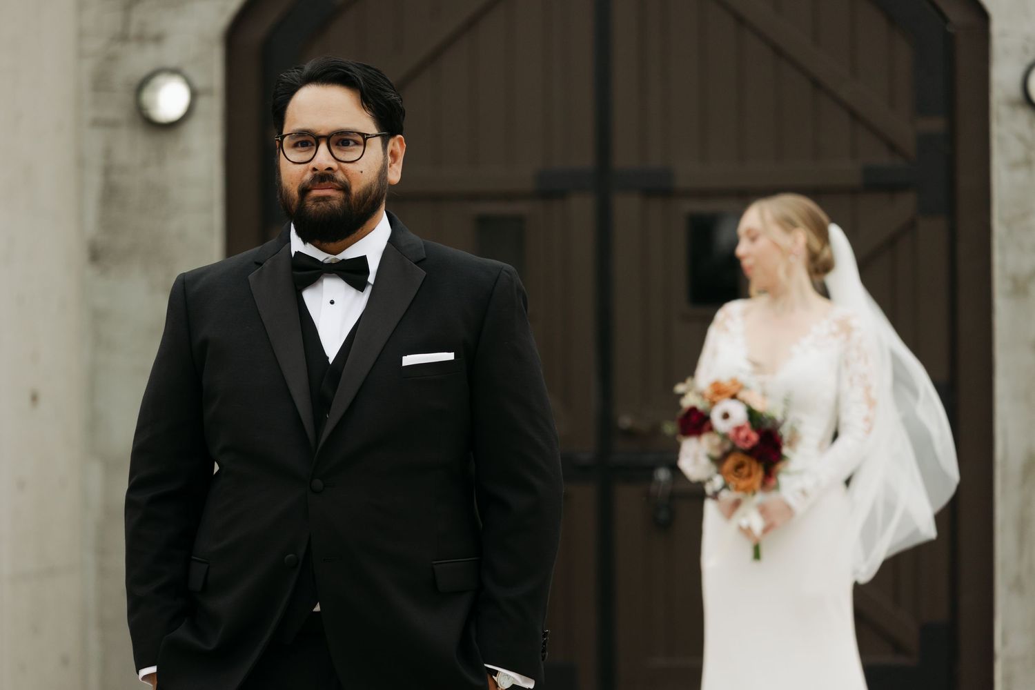 A couple at their wedding ceremony, with the groom in a black tuxedo and bride in white holding a bouquet at Lightfoot & Wolfville.