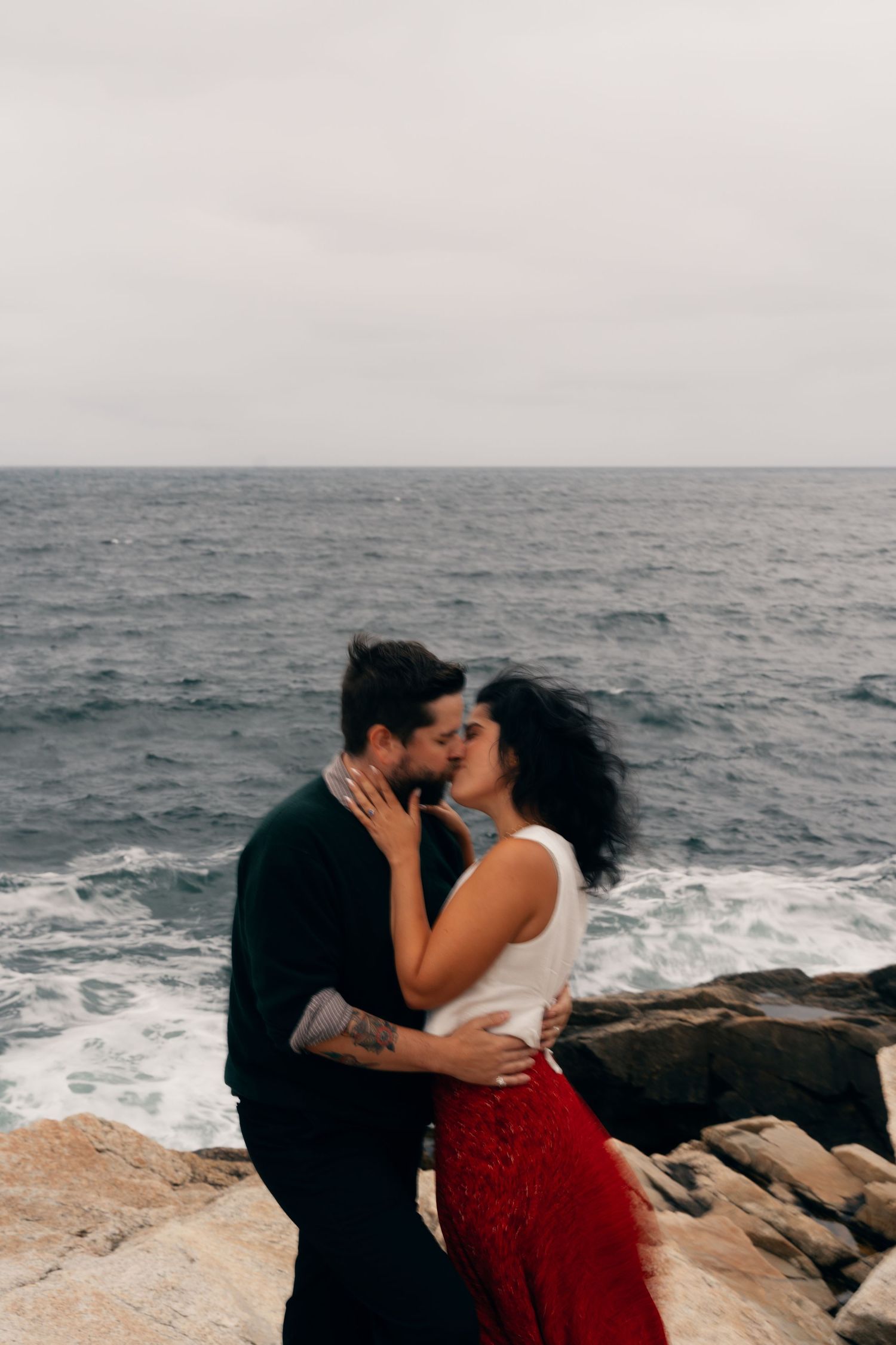 A couple shares romantic kisses on rocky coastal cliffs overlooking the ocean in Halifax, Nova Scotia in a series of intimate photos.