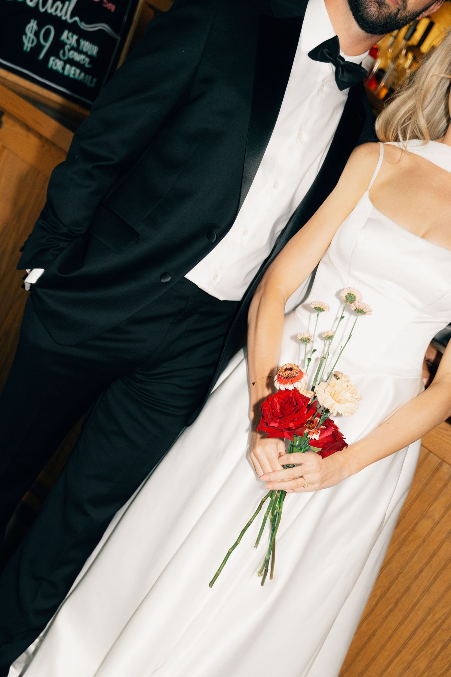 Close-up of wedding attire showing white dress and black tuxedo with red flower bouquet details in Halifax, Nova Scotia.