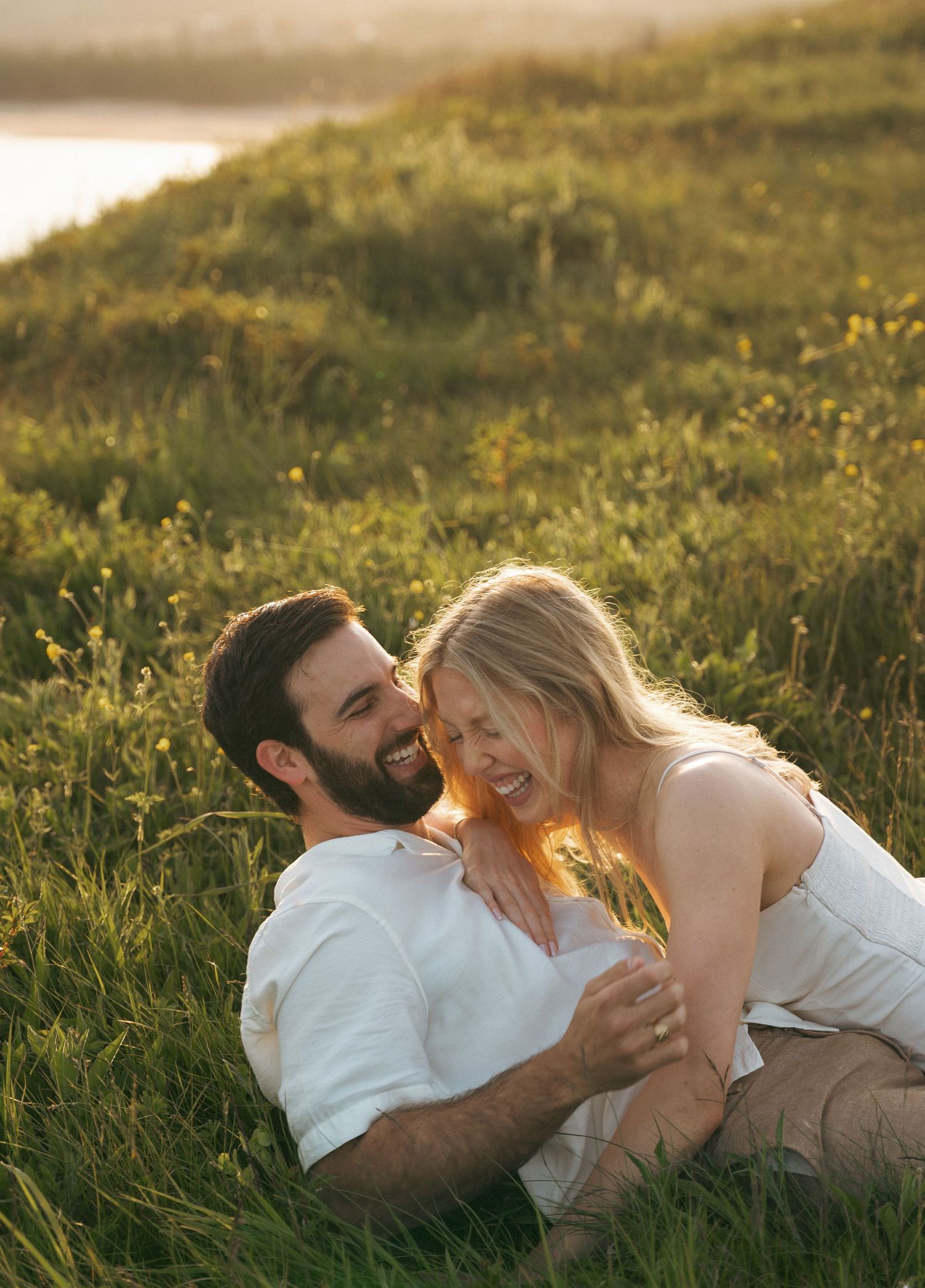 A couple shares intimate moments while laying in a sunlit meadow in Halifax, Nova Scotia during golden hour.