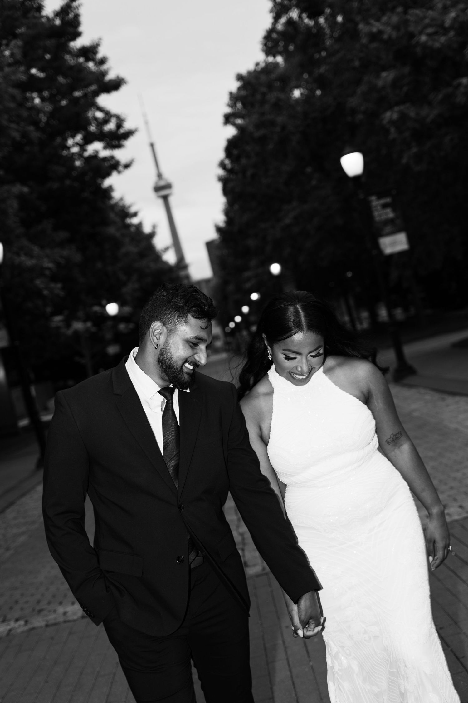 A couple in formal attire, with the person in white wearing a dress and the person in black wearing a suit, walking together in Toronto, ON.