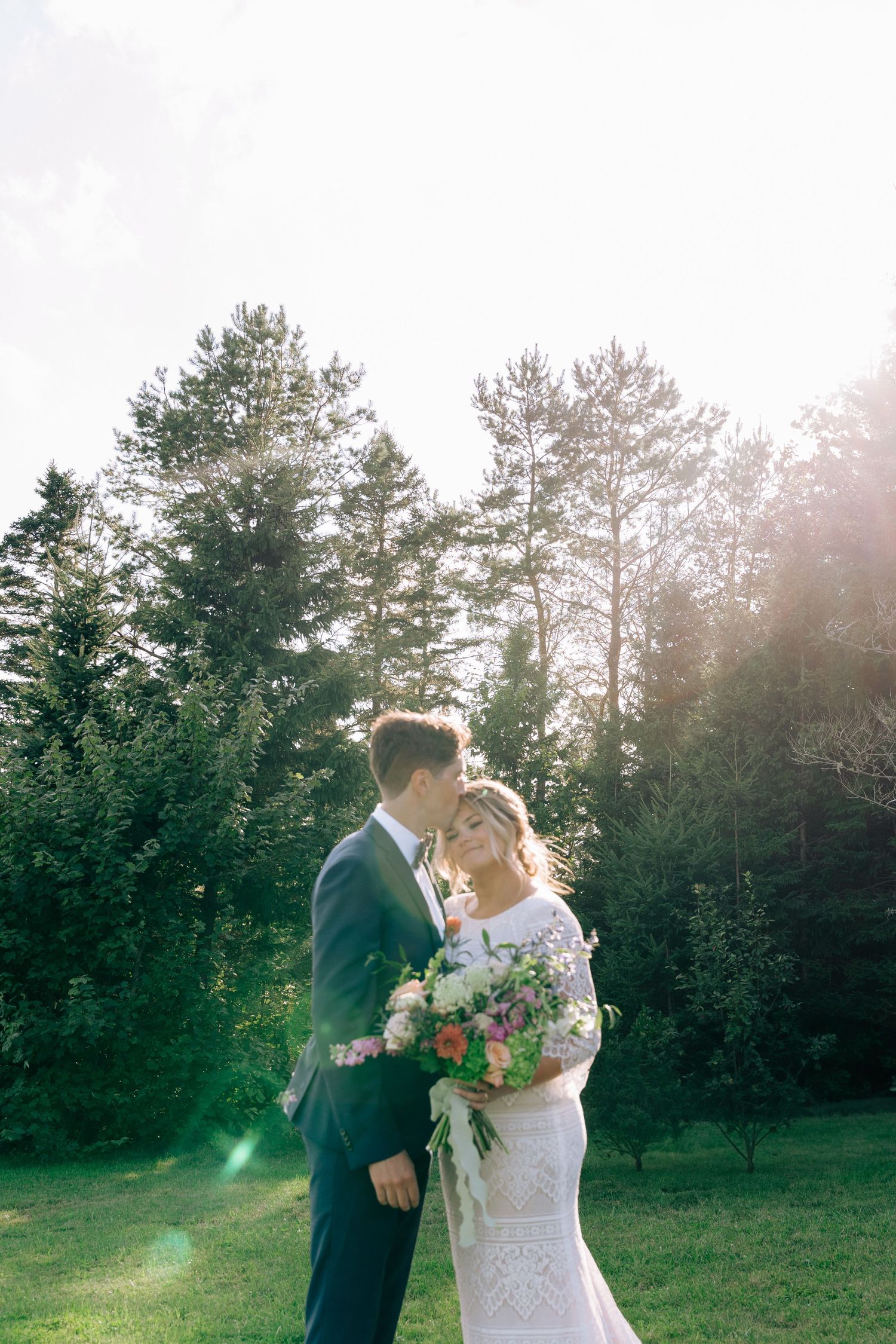 A romantic wedding couple embraces in a sun-drenched forest clearing during golden hour in Halifax, Nova Scotia.
