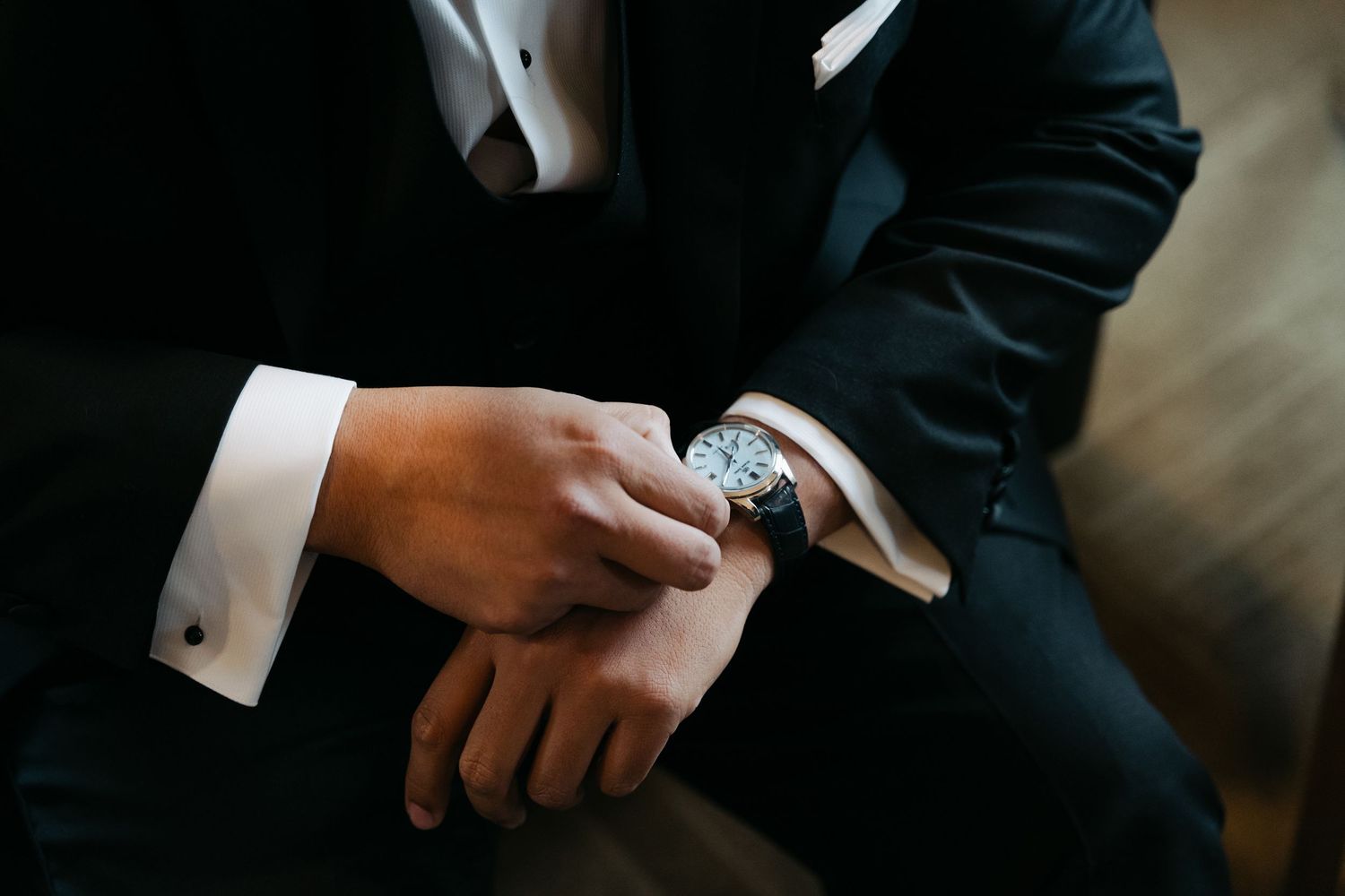 Close-up view of hands checking time on an elegant wristwatch while wearing formal business attire at Lightfoot & Wolfville.