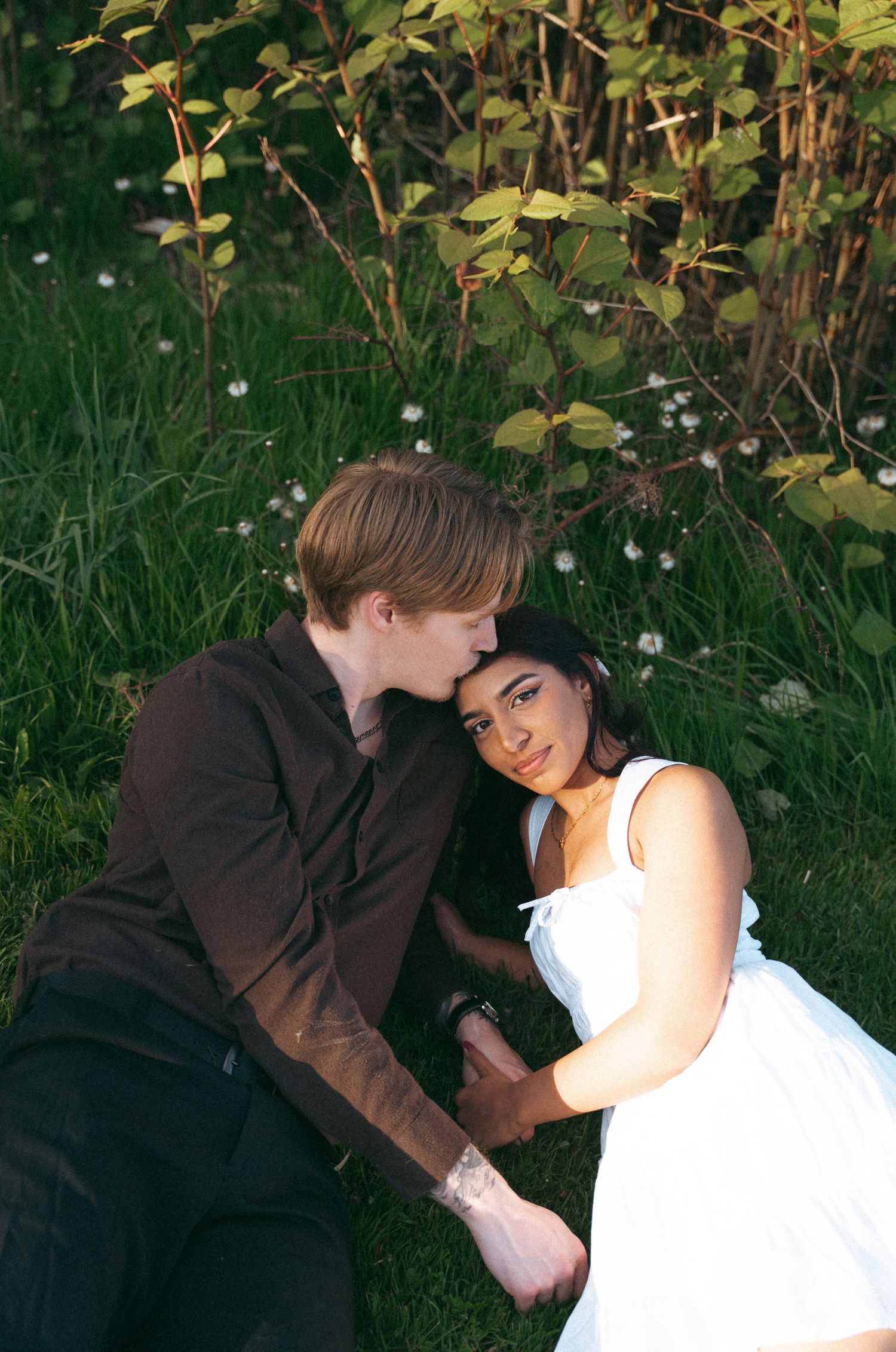 A romantic couple embraces in a garden setting in Halifax, Nova Scotia with green foliage and white flowers in the background.