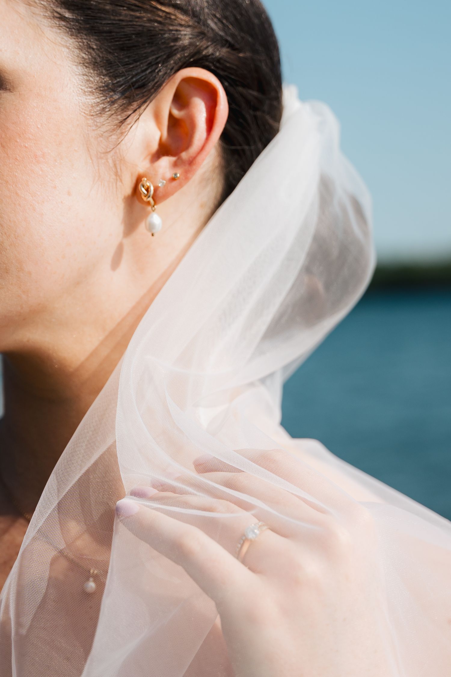 A delicate white wedding veil flows in the breeze against a blue sky and water backdrop in Halifax, Nova Scotia.