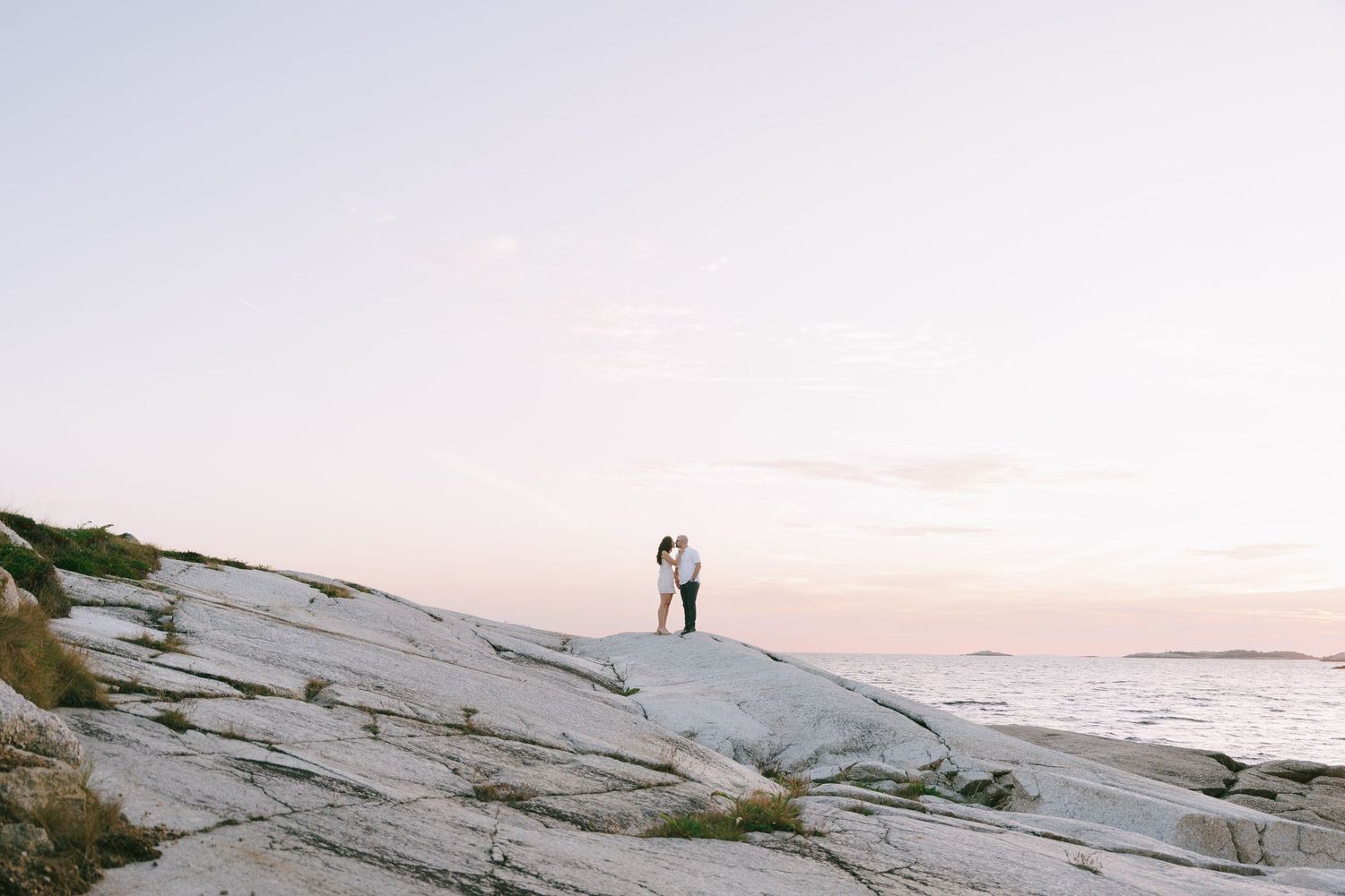 A couple poses on a rocky coastal cliff overlooking the ocean during sunset in Halifax, Nova Scotia.