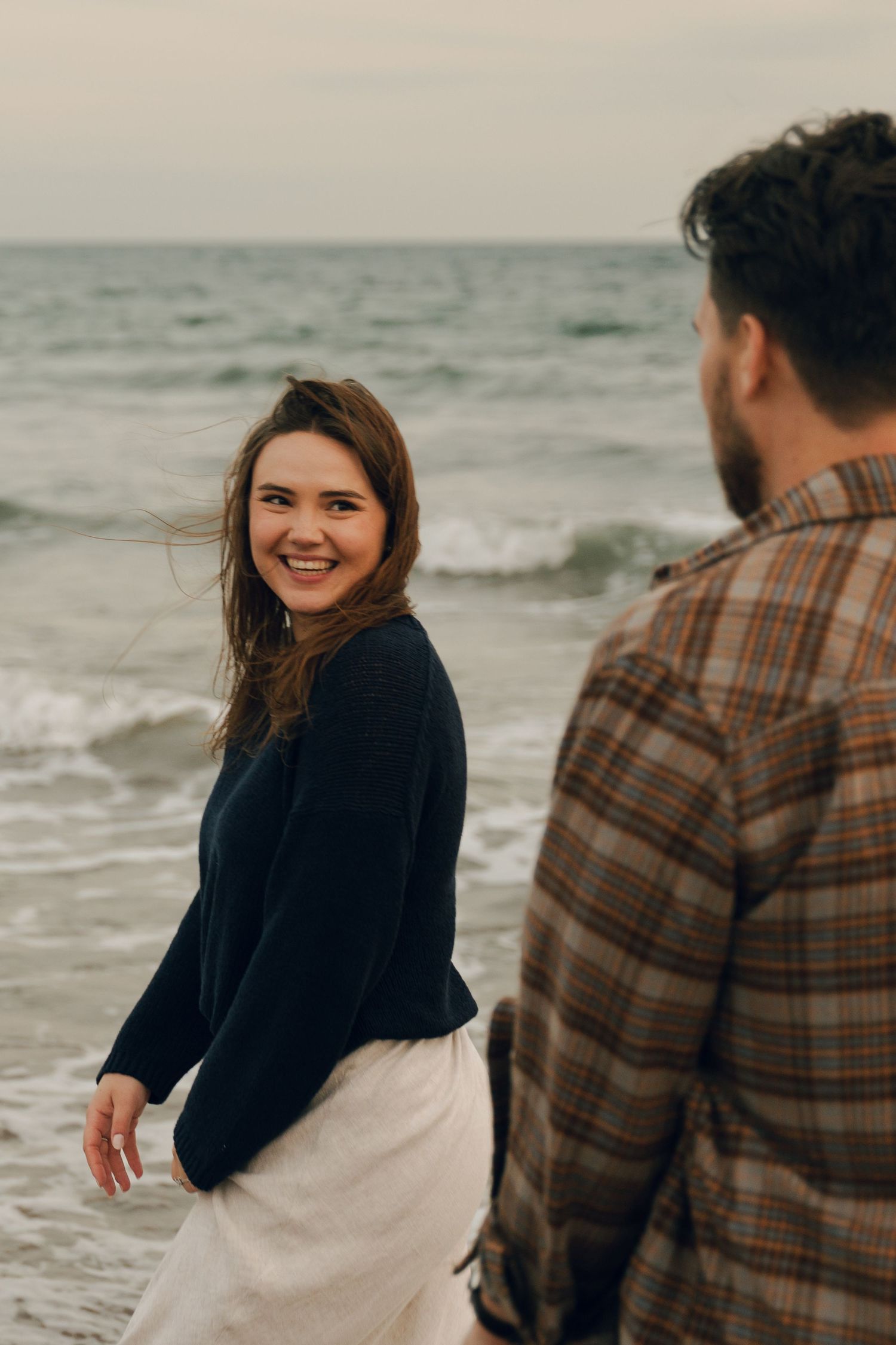 A couple shares a romantic moment on a cloudy beach with waves crashing behind them in Halifax, Nova Scotia.