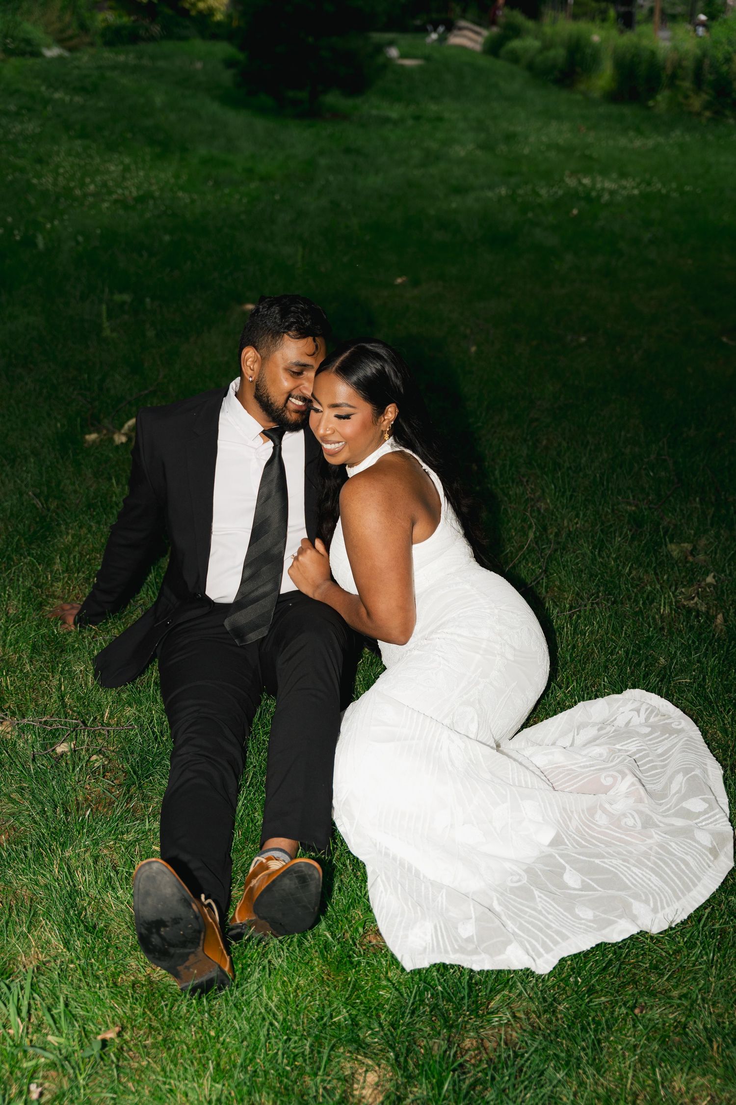 A couple in wedding attire shares an intimate moment while sitting together on green grass in Toronto, Ontario.