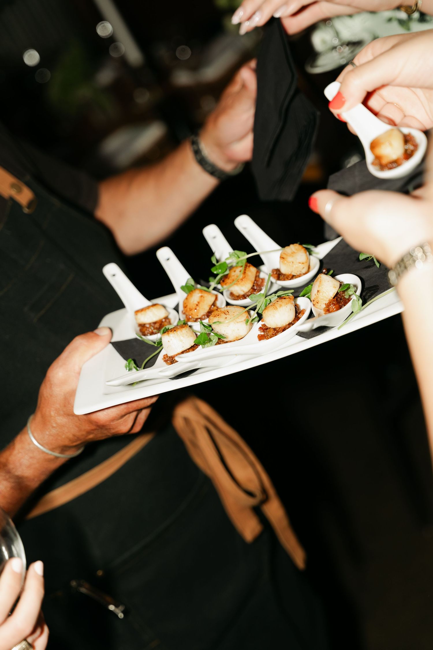 Hands passing elegant appetizer plates with garnished hors d'oeuvres at an upscale event in dark lighting in Halifax, Nova Scotia.