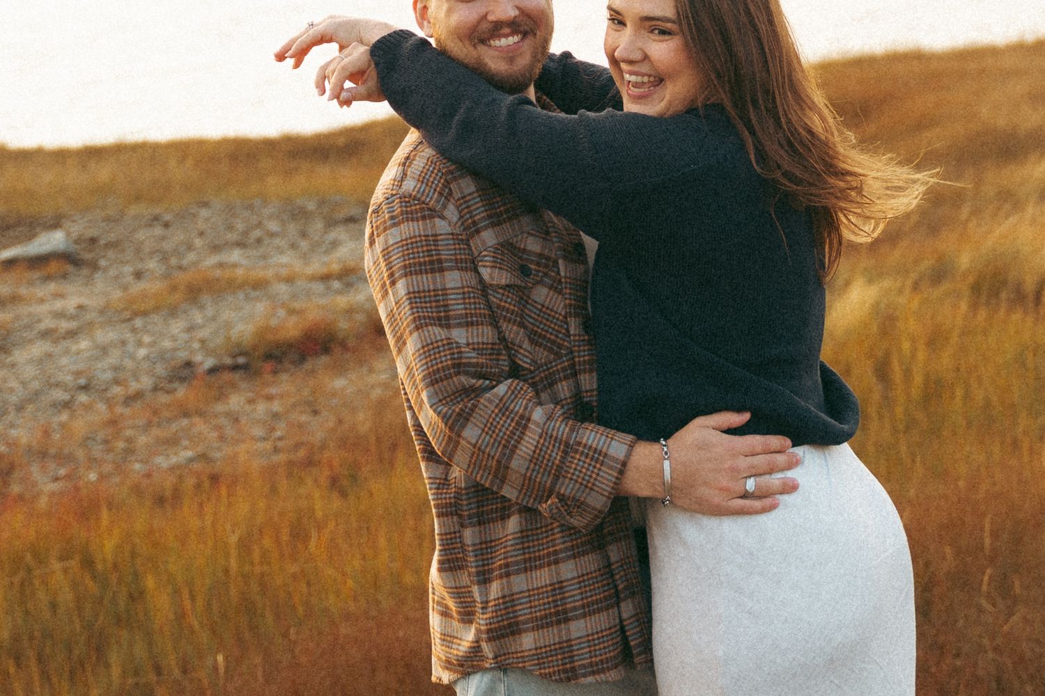 A couple embraces during a romantic sunset photoshoot in a golden field of tall grass in Halifax, Nova Scotia.