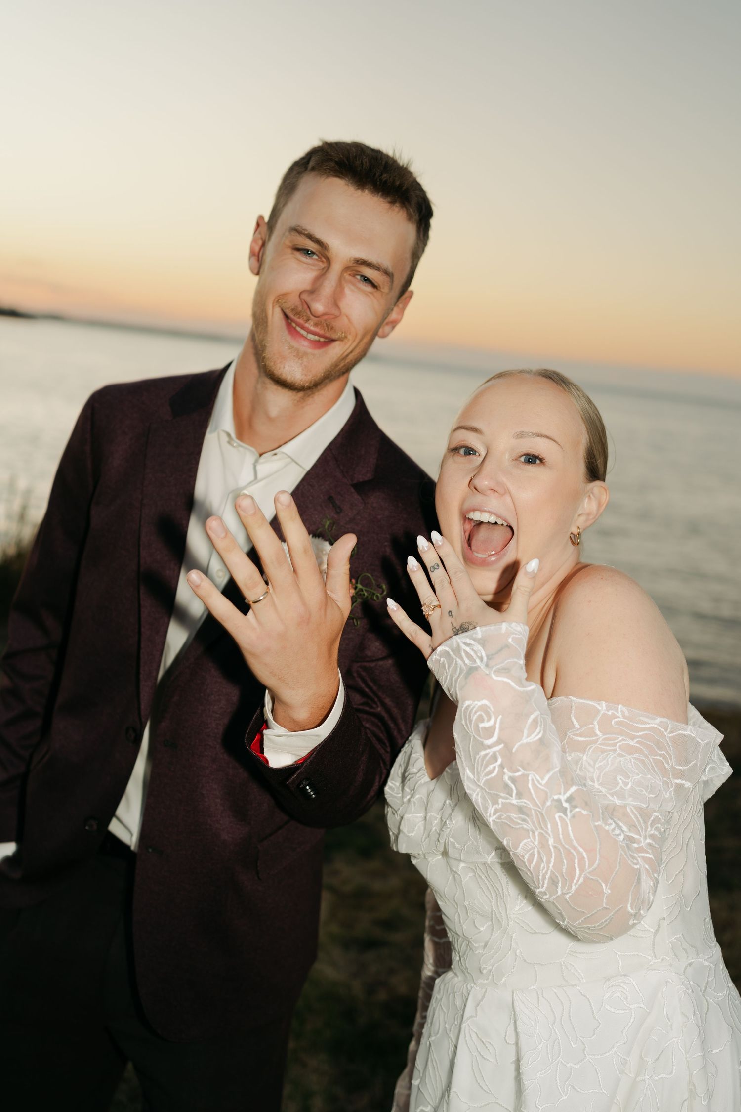 Couple poses playfully at sunset by the water showing off their wedding rings in Nova Scotia.