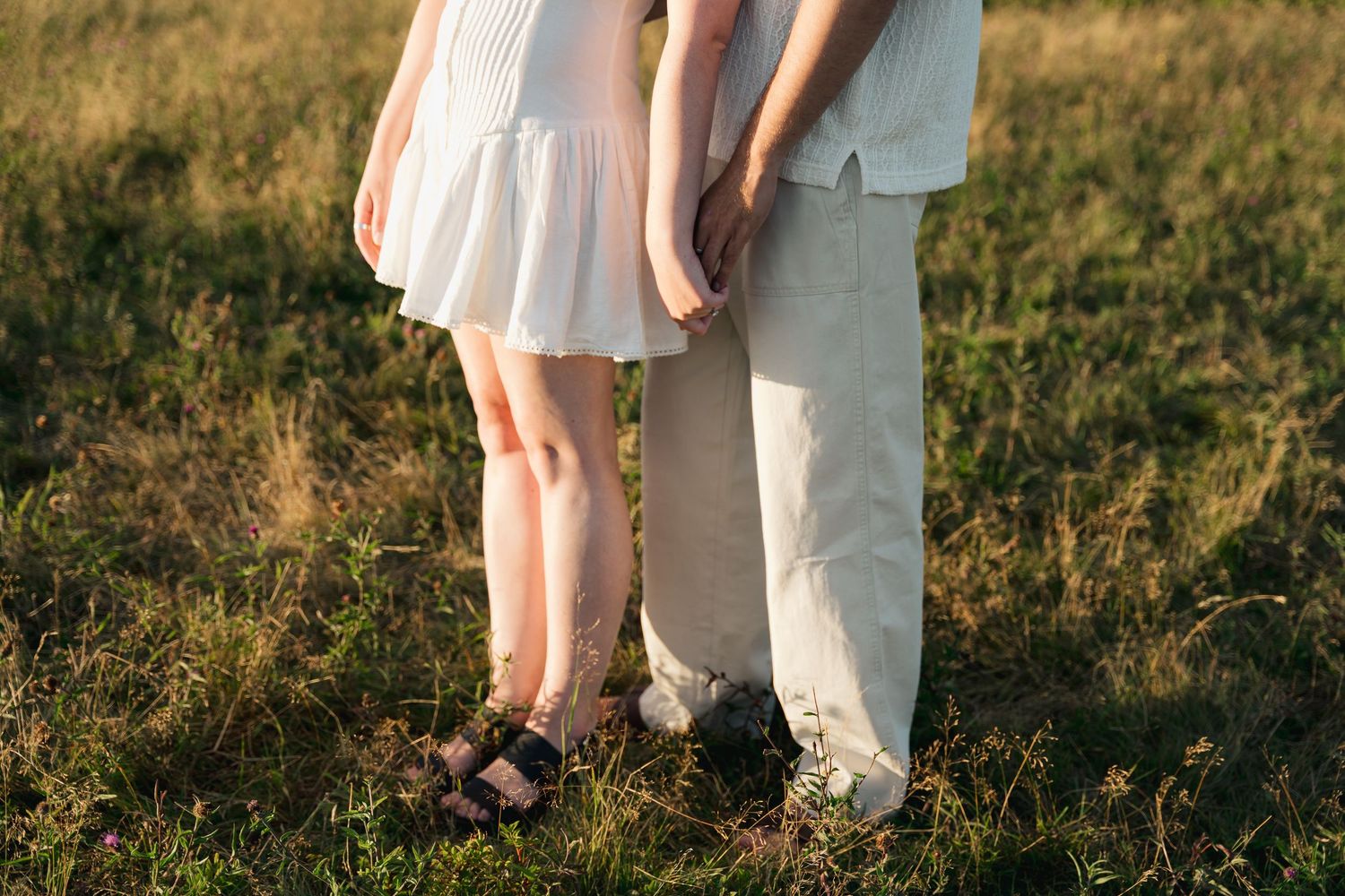 Couple in white outfits walking through a sunlit grassy field in Halifax, Nova Scotia during golden hour.