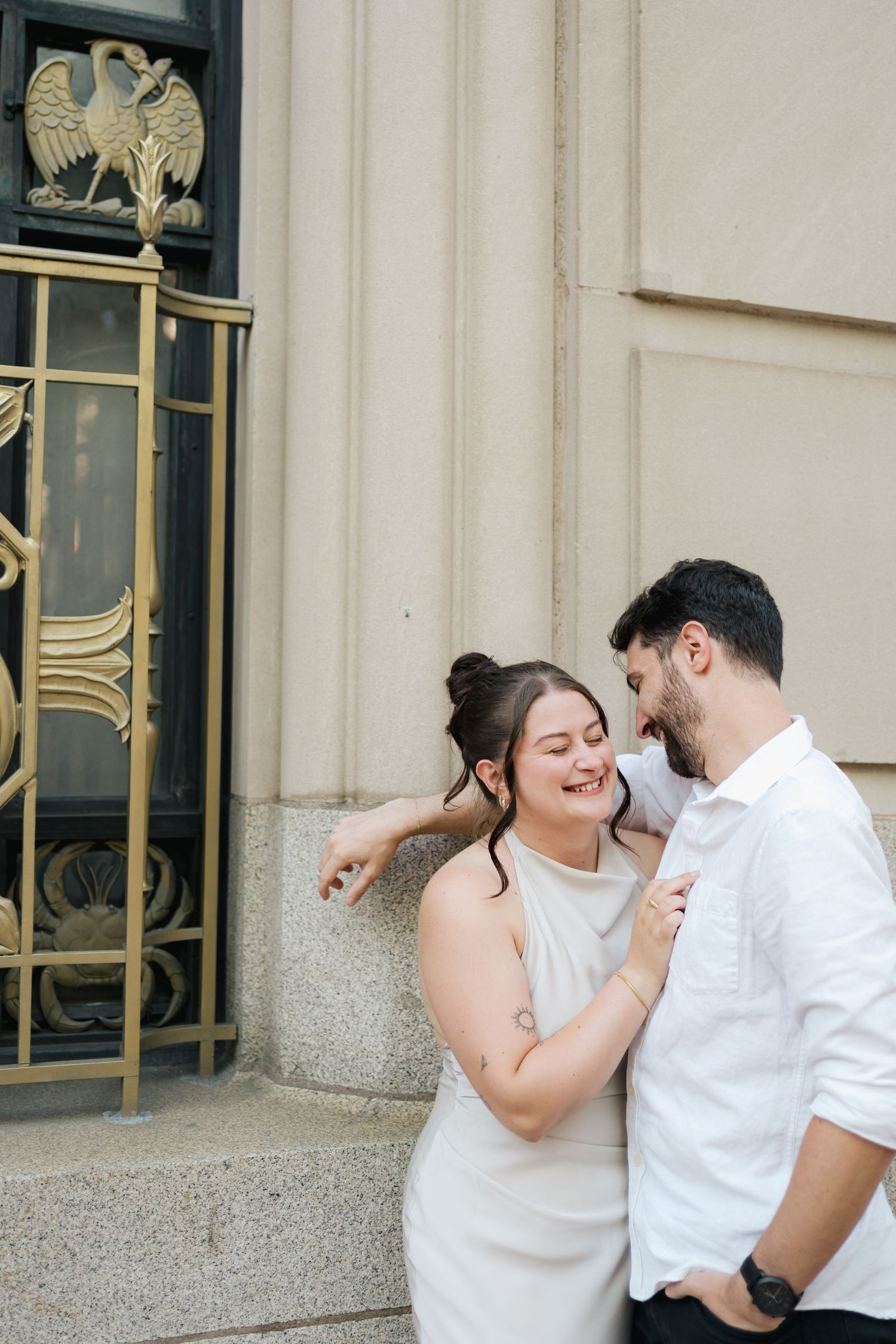 A couple shares a joyful moment together outside a building with ornate architectural details and a decorative eagle in Halifax, Nova Scotia