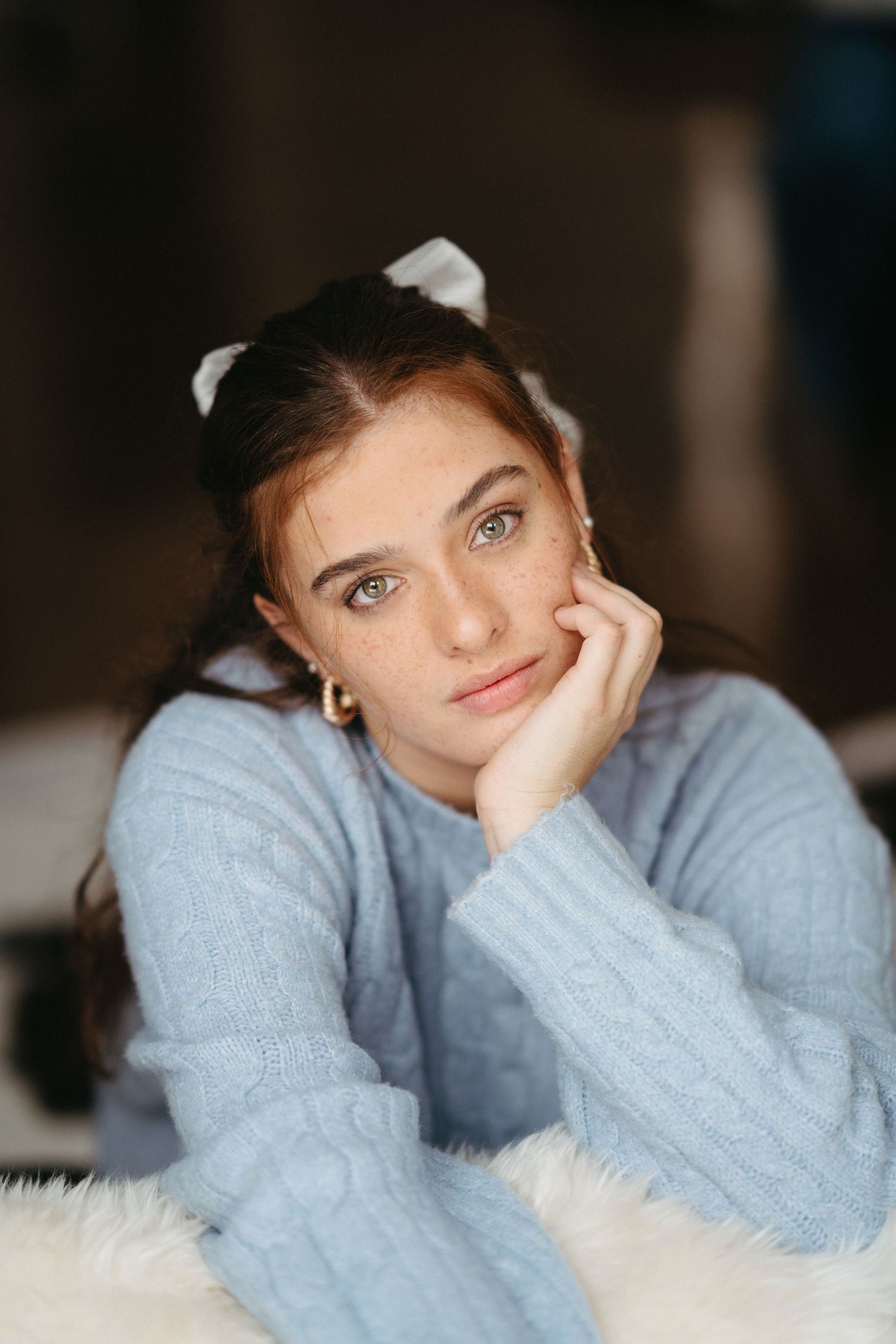 A person in a cozy light blue sweater poses thoughtfully on a white fluffy surface in a series of expressive portraits in Halifax, NS