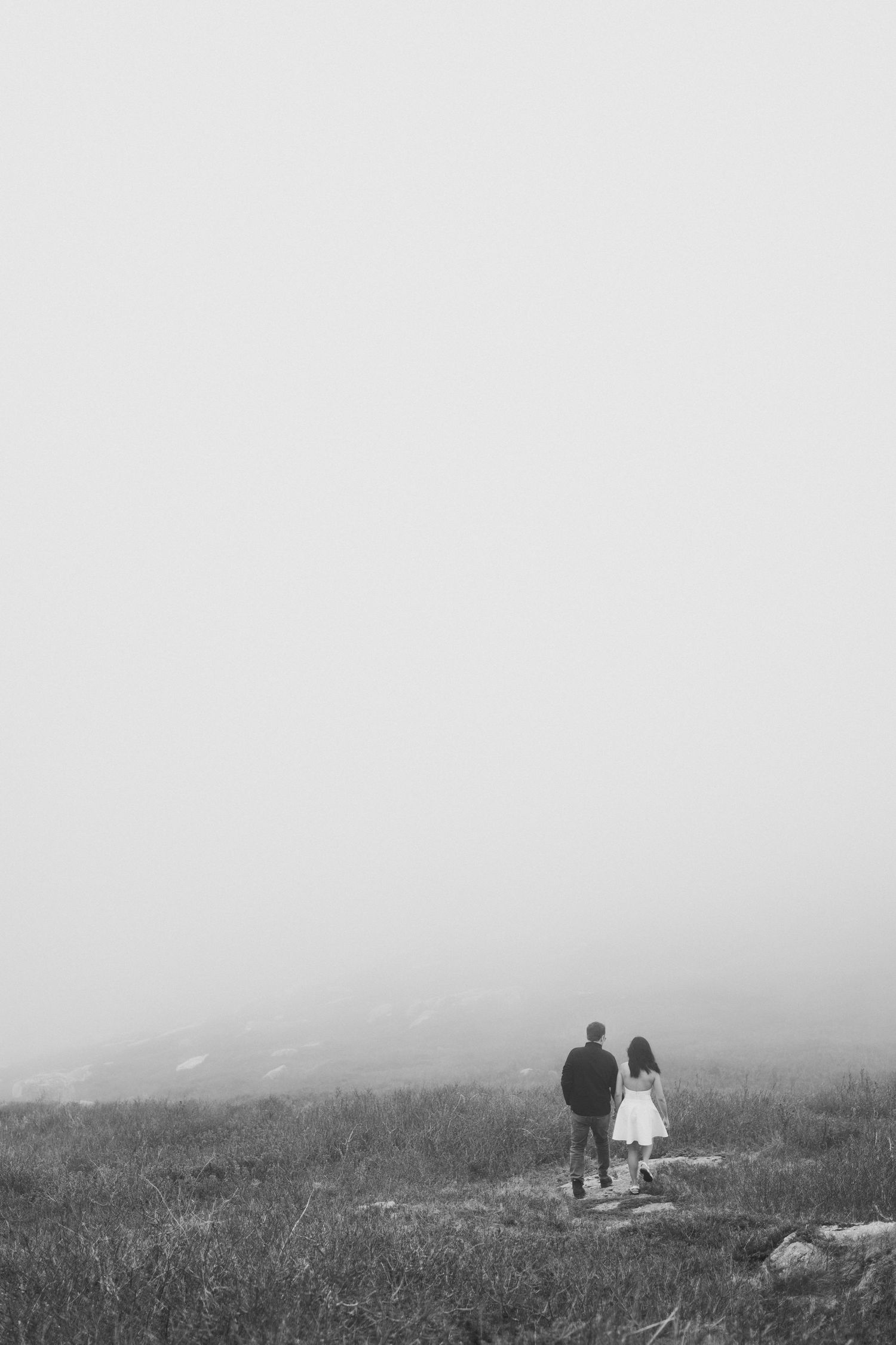 Two silhouetted figures walk together through a misty hillside landscape in black and white in Halifax, Nova Scotia.