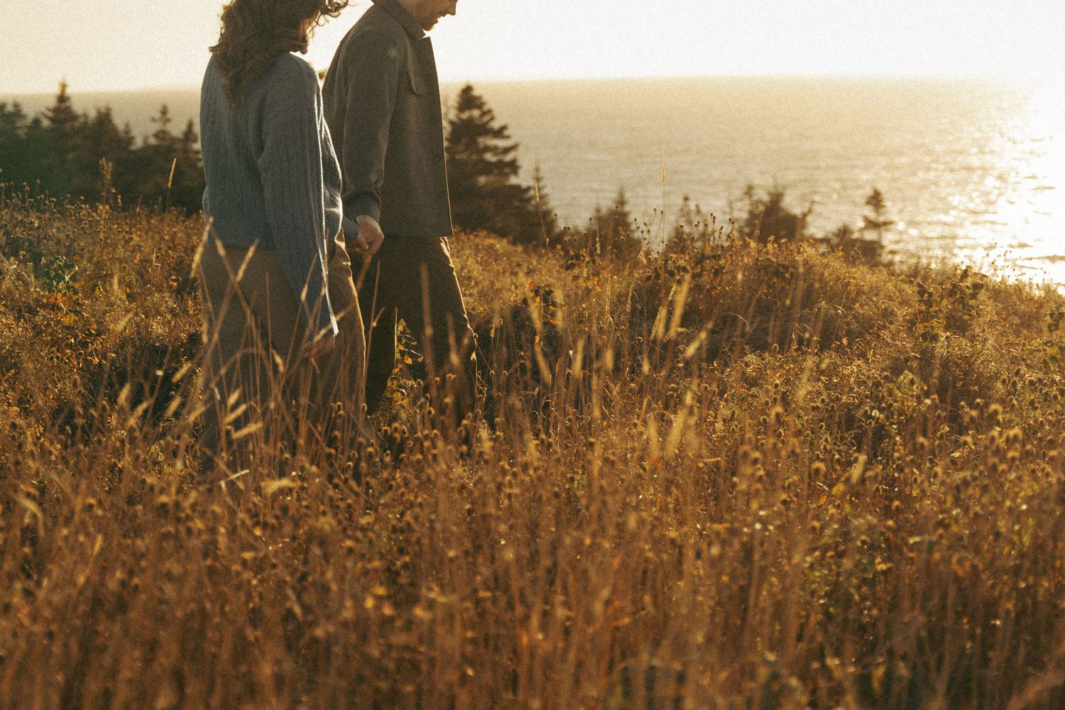 A silhouetted figure stands on a grassy coastal cliff at golden hour as sunlight sparkles on the ocean below in Halifax, Nova Scotia.