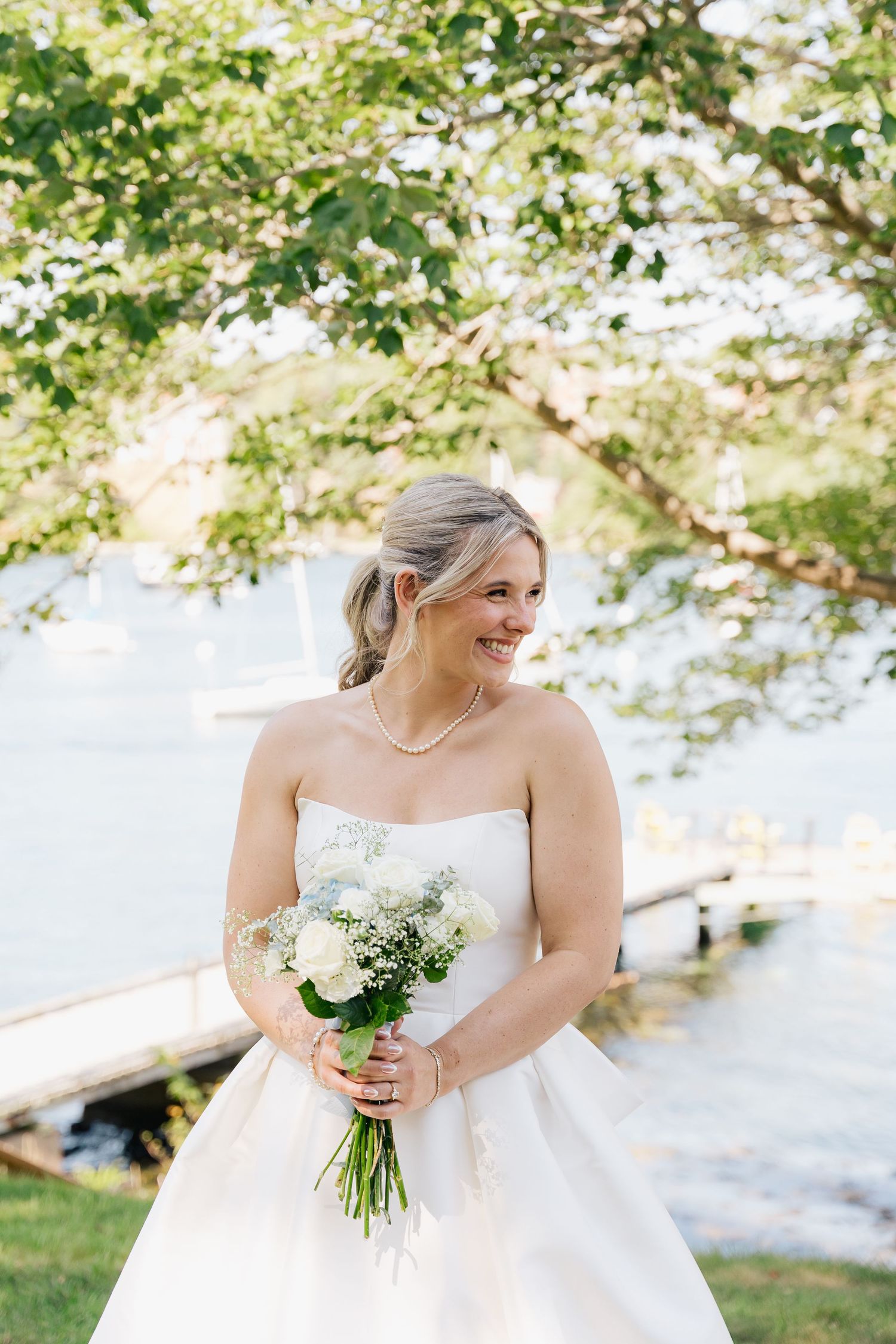 Bride in white dress holding a delicate bouquet of flowers against a sunny outdoor backdrop in Halifax, Nova Scotia.