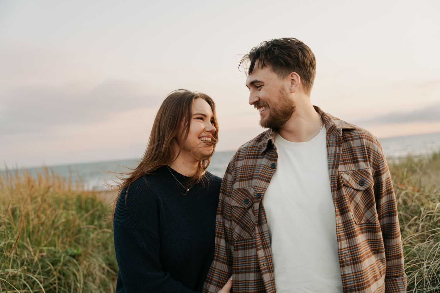 A couple shares joyful laughter while standing together outdoors during golden hour in Halifax, Nova Scotia.