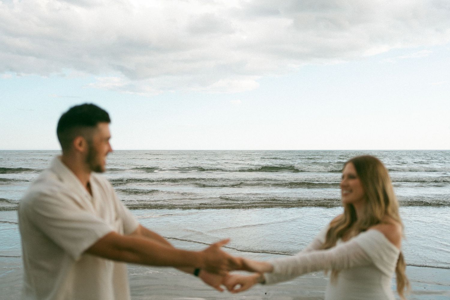 A couple dances and spins together on a cloudy beach during sunset, creating romantic silhouettes against the ocean in Halifax, Nova Scotia.