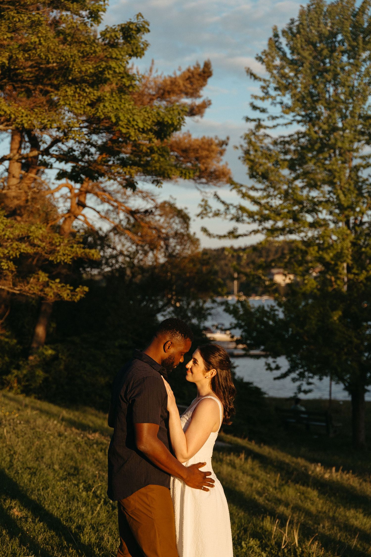A romantic sunset moment between two people embracing on a grassy hillside with autumn trees in the background in Halifax, Nova Scotia.