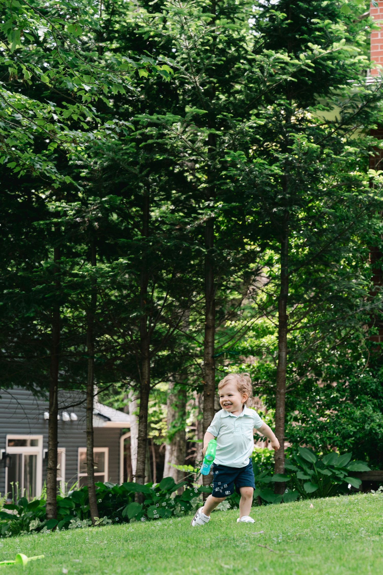 Children playing and running together on a grassy hill surrounded by tall green trees on a sunny summer day in Halifax, Nova Scotia.