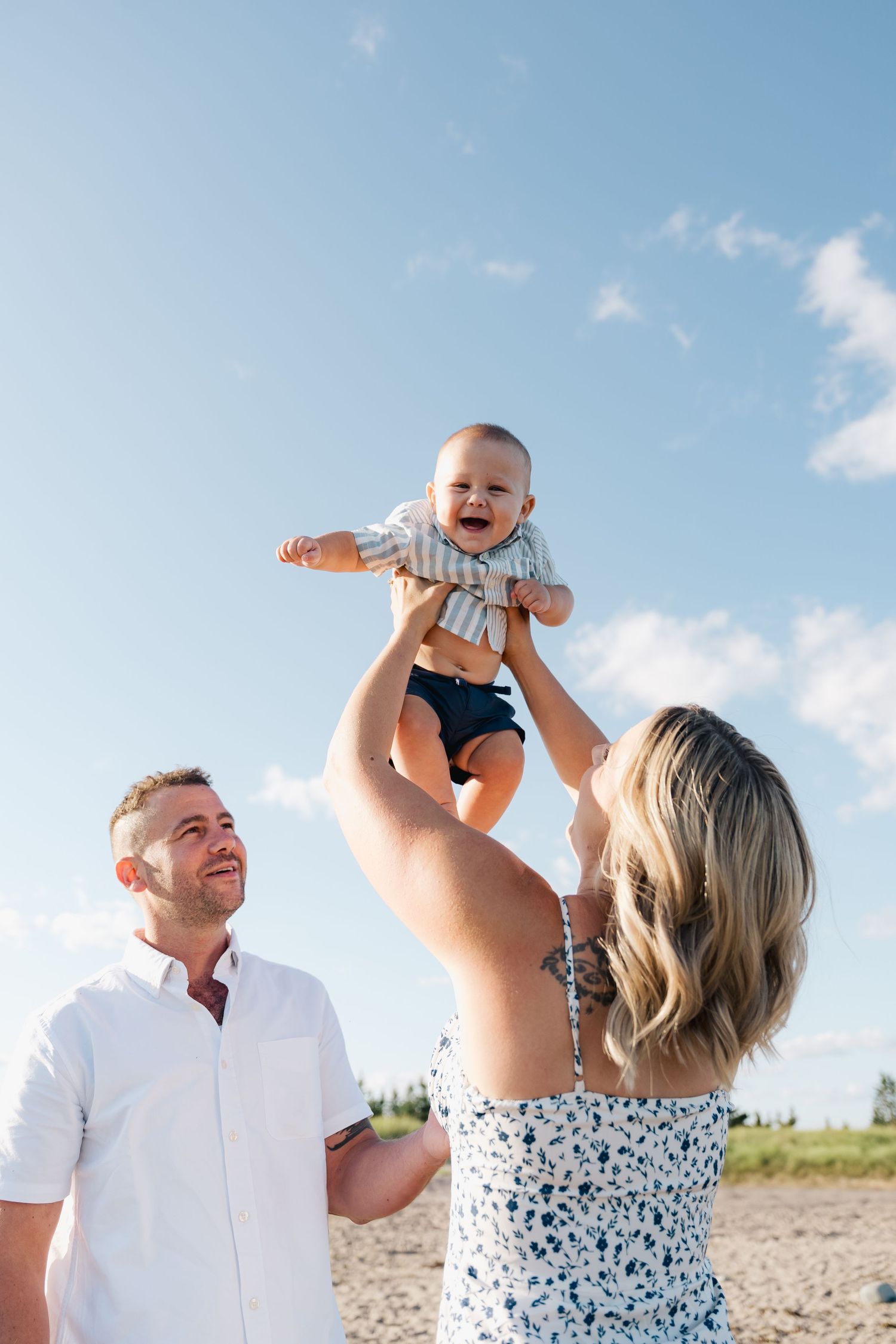 A series of candid photos showing a couple in white clothing playing with a baby against a blue sky background in Halifax, Nova Scotia.