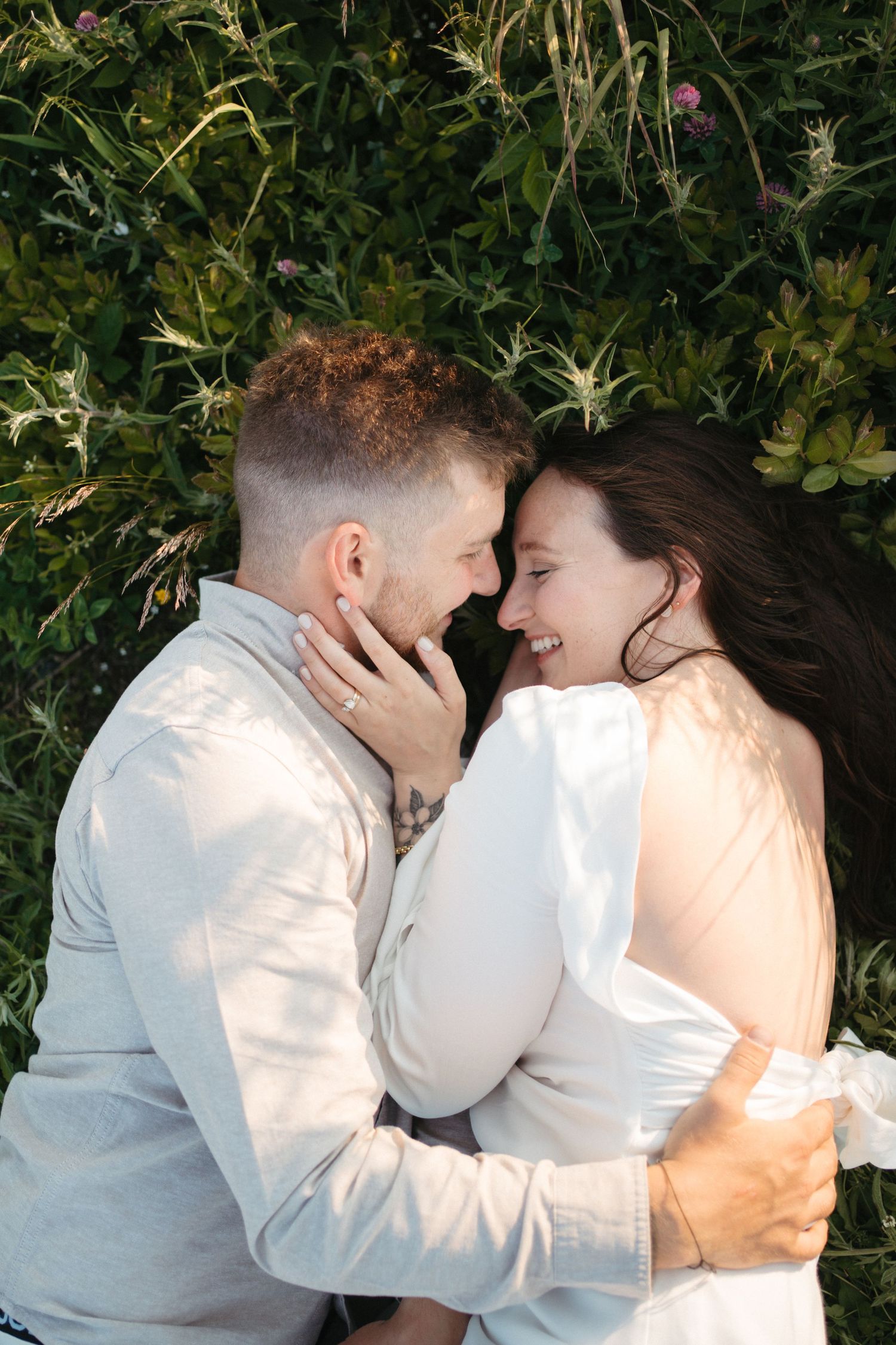 A romantic couple in white outfits share intimate moments against a lush green foliage backdrop in Halifax, Nova Scotia.