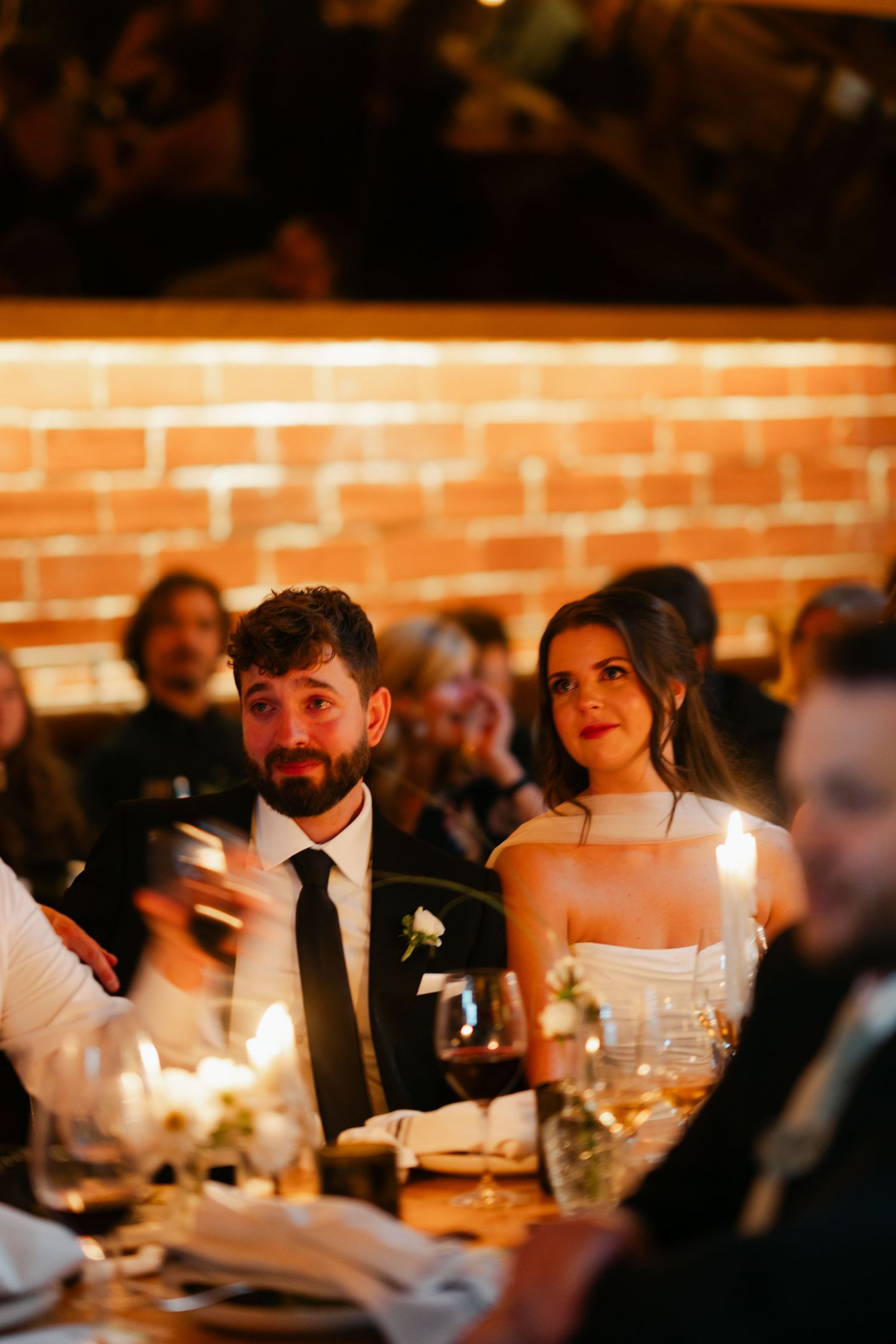 A candlelit wedding reception dinner with guests seated at tables in a rustic brick-walled venue at Halifax, Nova Scotia.