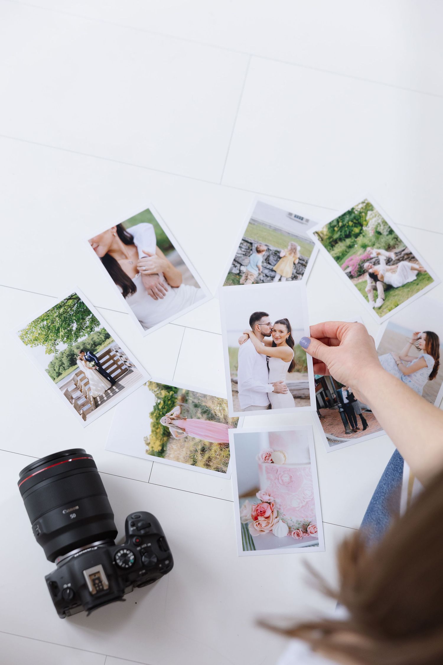 Overhead view of a photographer reviewing printed wedding photos on a white floor next to a Canon DSLR camera.