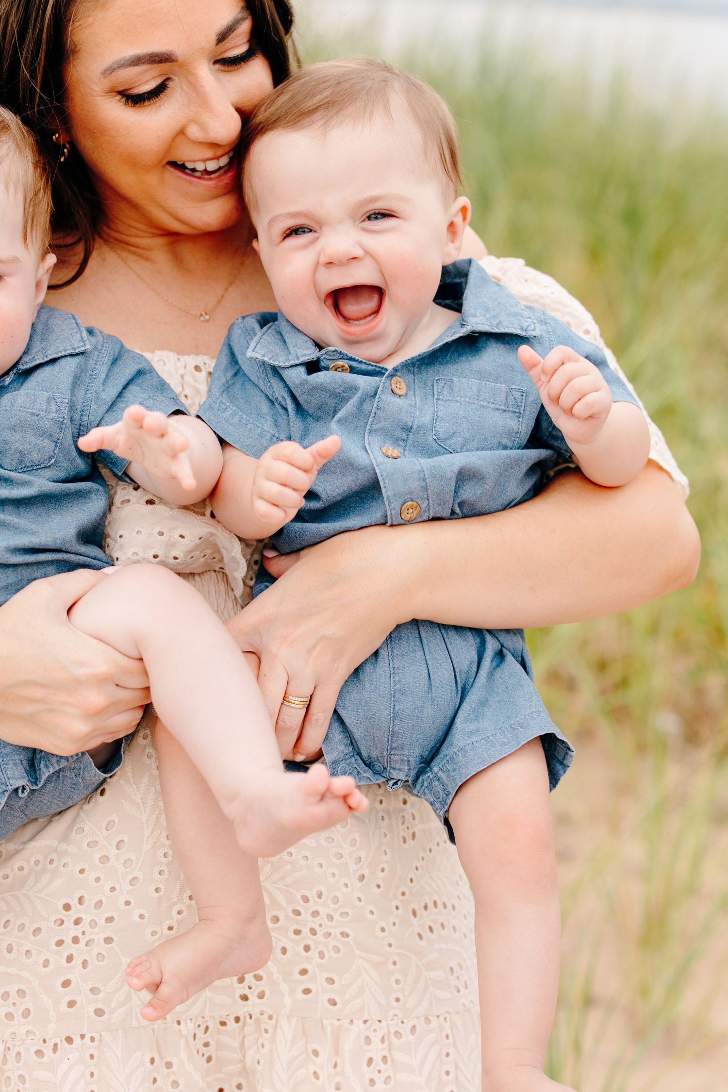 Laughing baby in denim romper held by smiling mother outdoors.