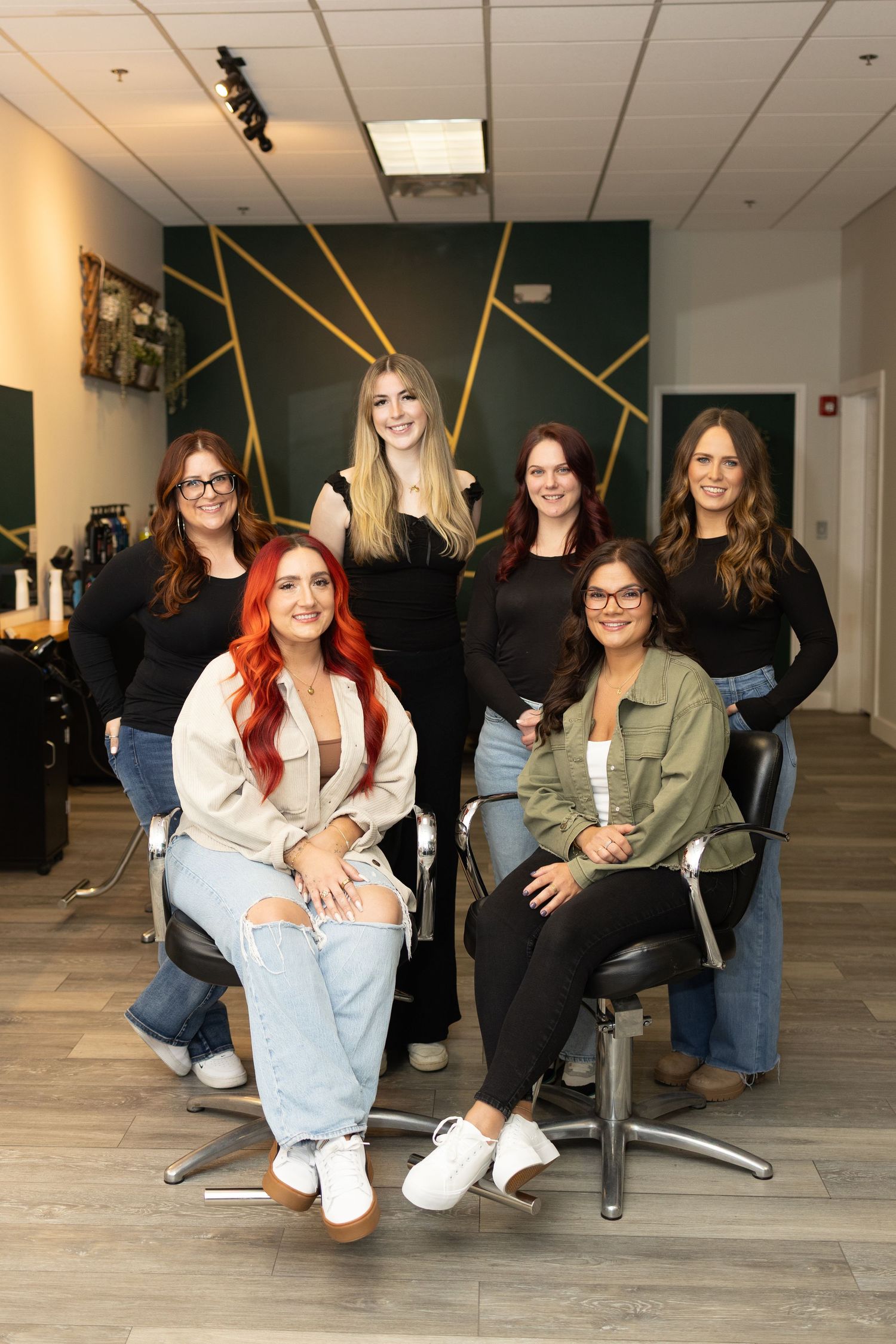 Group portrait of seven female salon professionals posing together in modern green and gold salon.