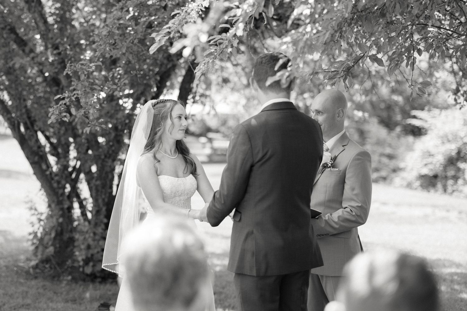 Black and white photo of bride and groom holding hands during intimate outdoor wedding ceremony.