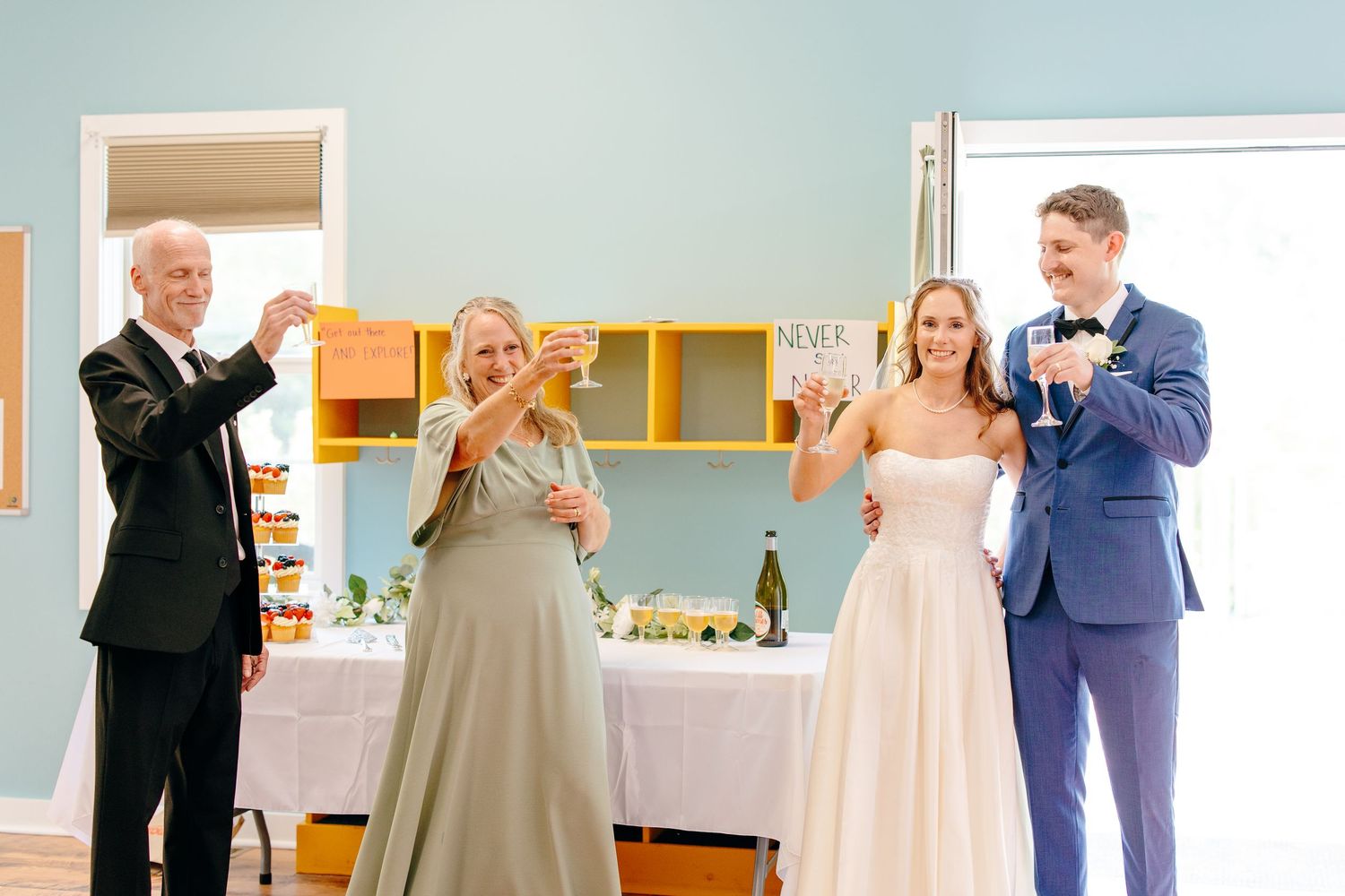 Bride and groom toast with champagne alongside two guests during a wedding reception in a bright venue.