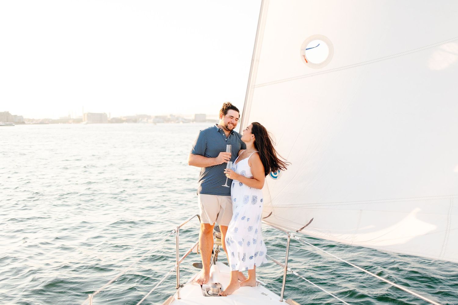 Happy couple celebrating on a sailboat deck with champagne and a city skyline behind them.