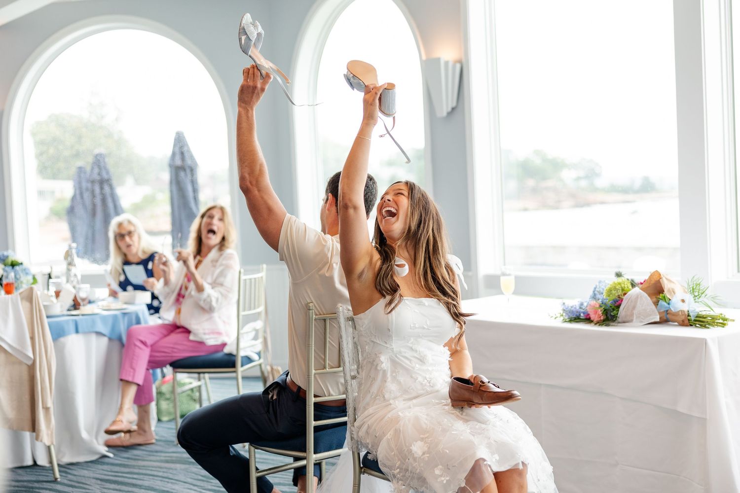 Joyful couple celebrating at a bridal shower, raising shoes in the air during a fun party game.