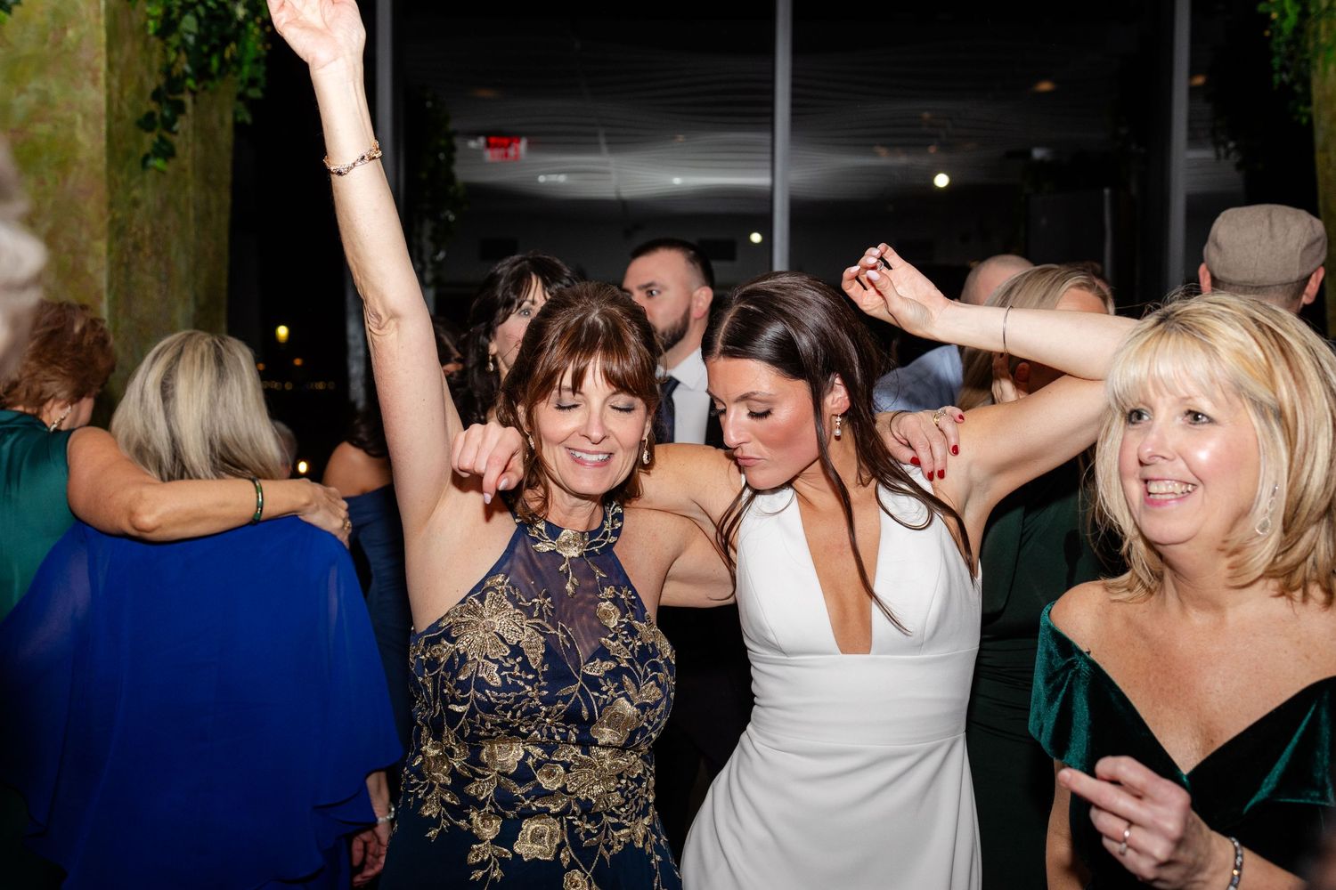 Bride and guests dance joyfully with arms raised at elegant wedding reception celebration.