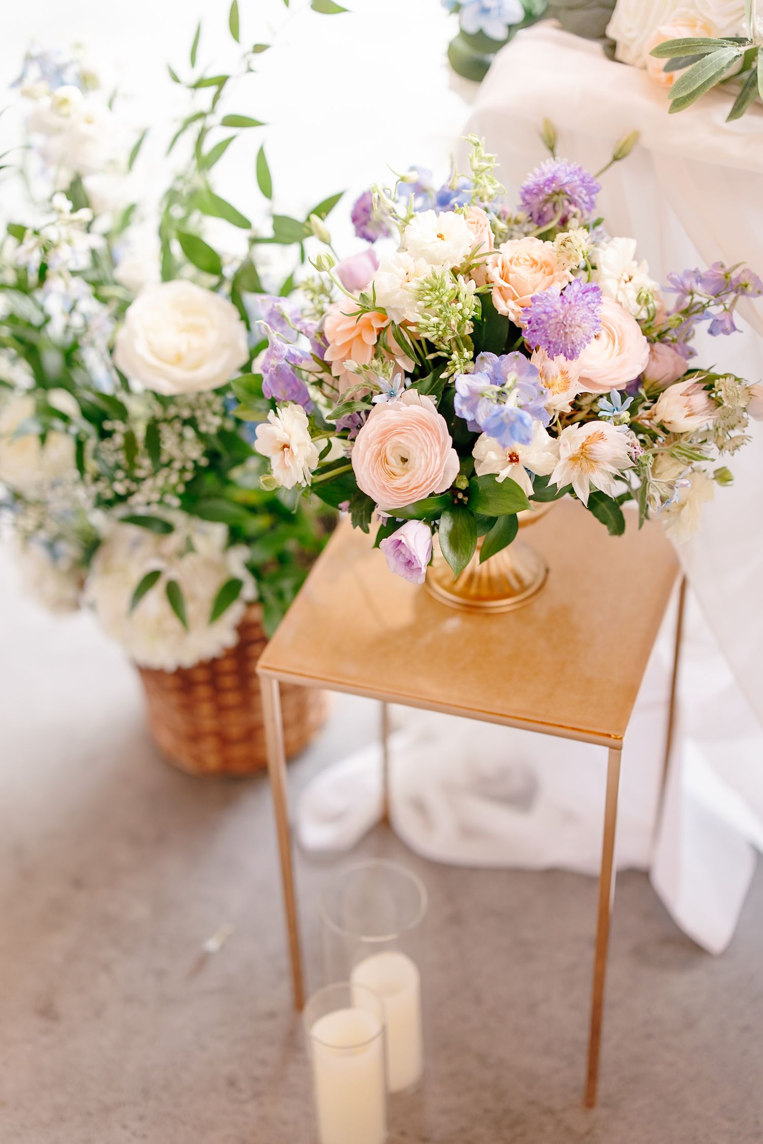Elegant wedding floral arrangement with peach roses and purple blooms on gold pedestal table.