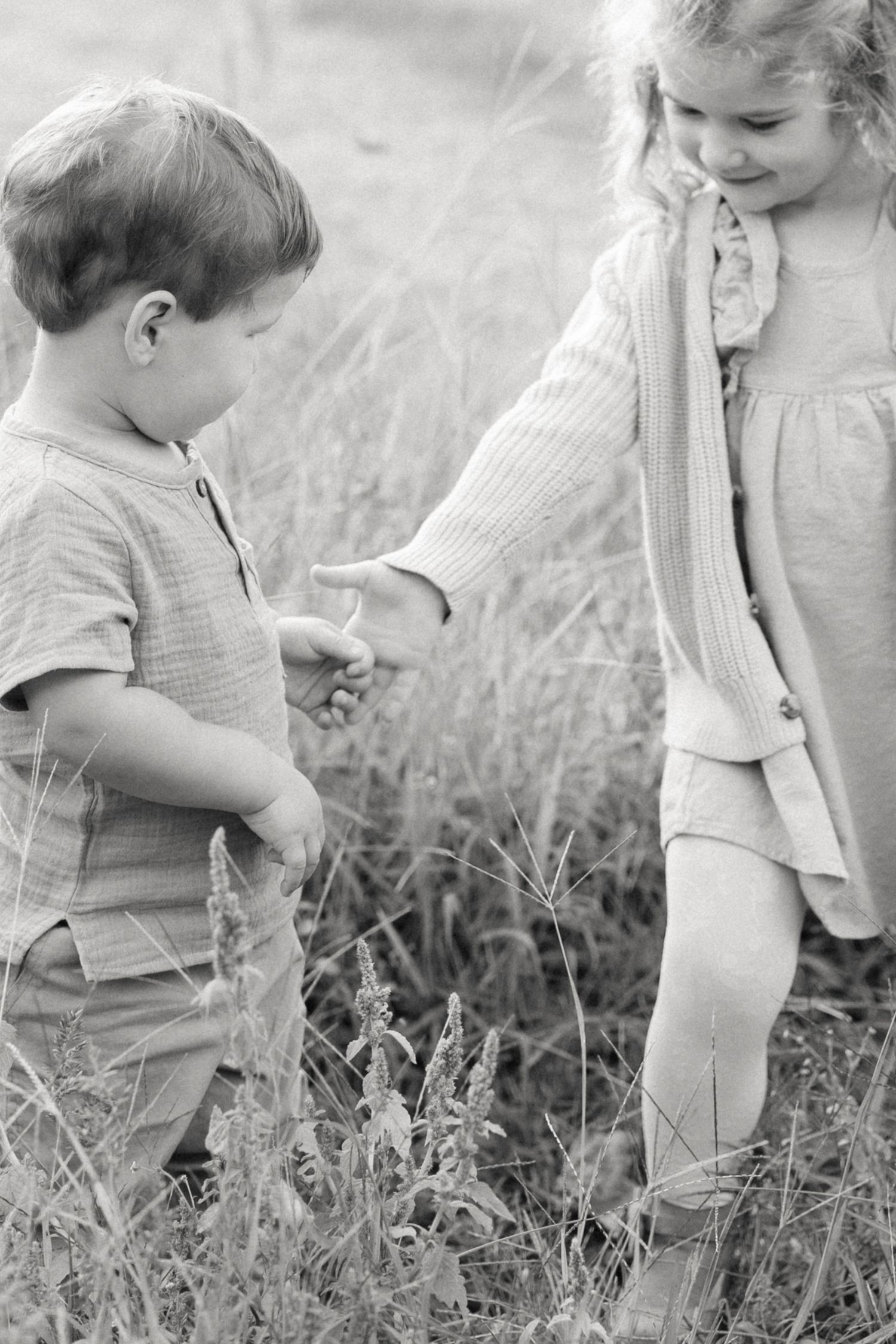 Black and white photo of two young children holding hands in a grassy meadow.