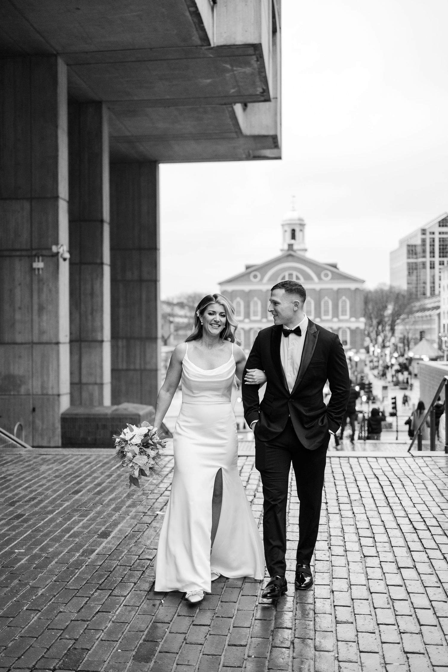 Black and white photo of bride and groom walking on brick path near Faneuil Hall Boston.