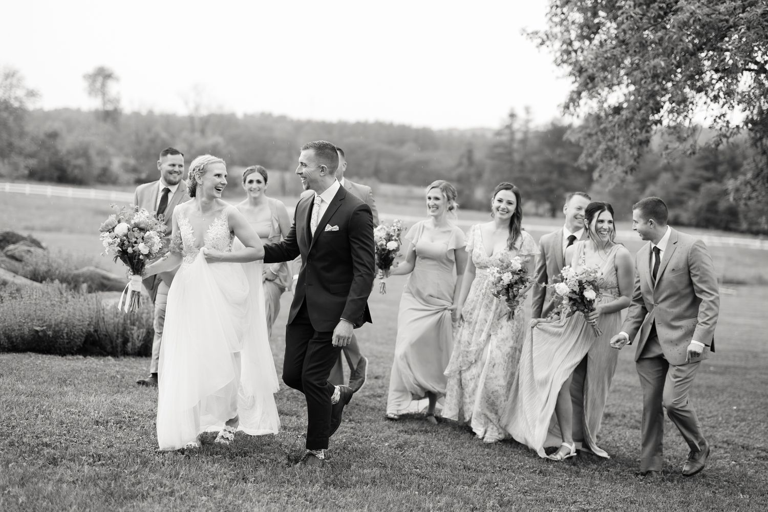 Wedding party walking and laughing together on a green lawn, black and white photo.