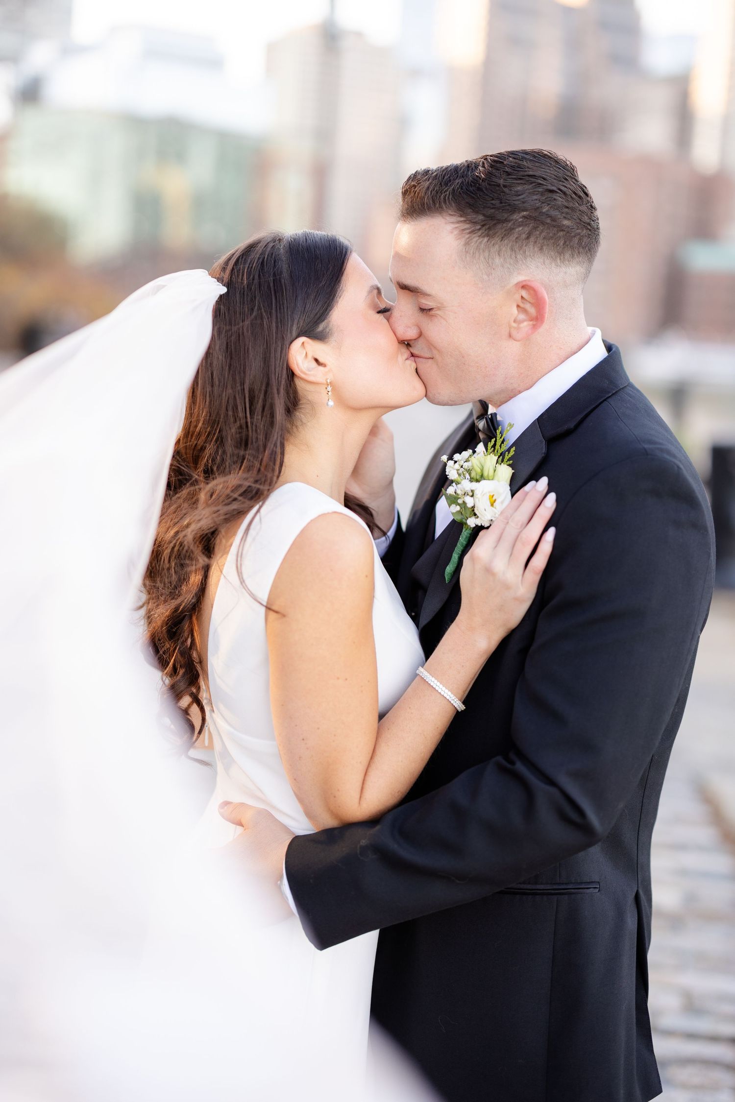 Bride and groom share a romantic kiss with city buildings softly blurred in the background.