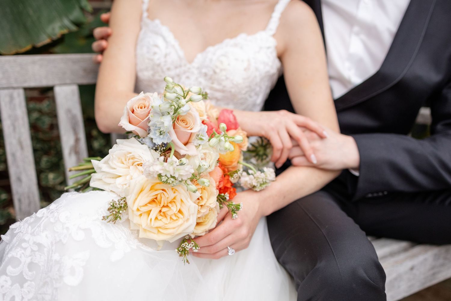Close-up of bride and groom hands with colorful peach and coral bridal bouquet.