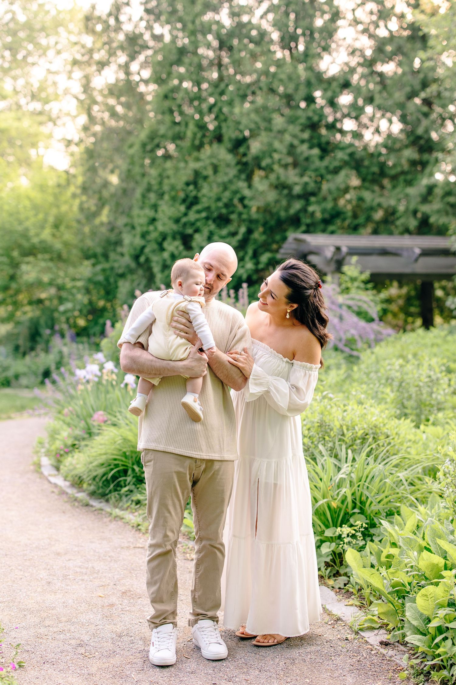Young family with baby strolling through lush garden at golden hour.