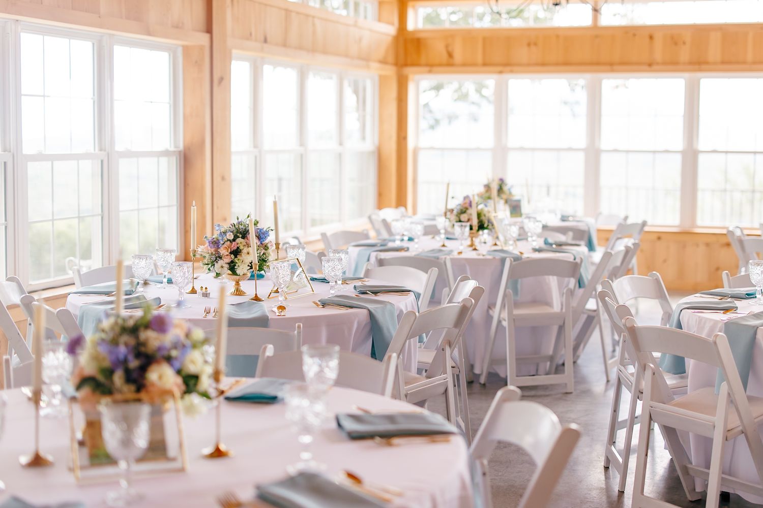 An elegant wedding reception venue with white tablecloths, floral centerpieces, and natural light streaming through large windows.