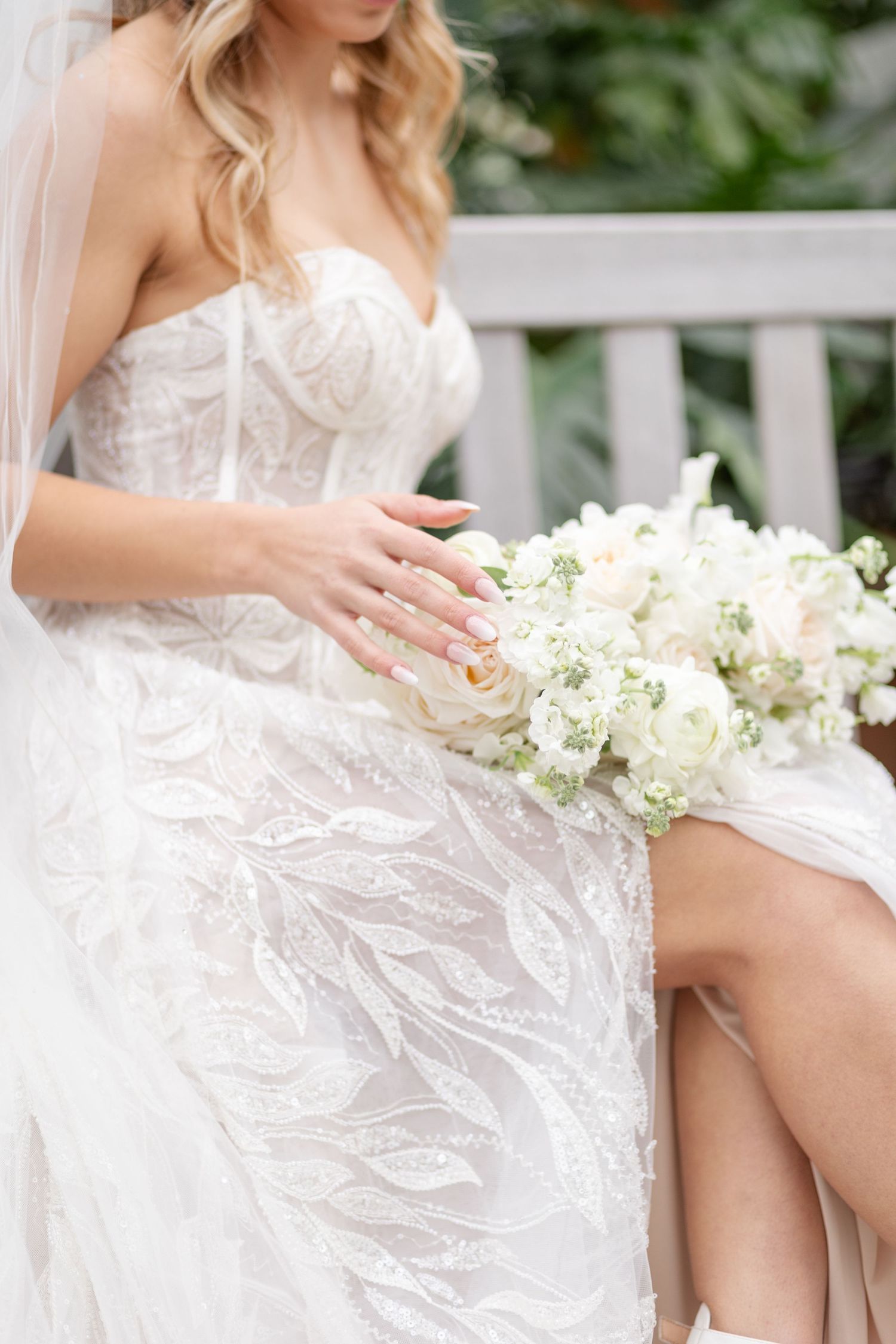 Detail shot of bride in lace strapless gown holding white rose bouquet on lap.